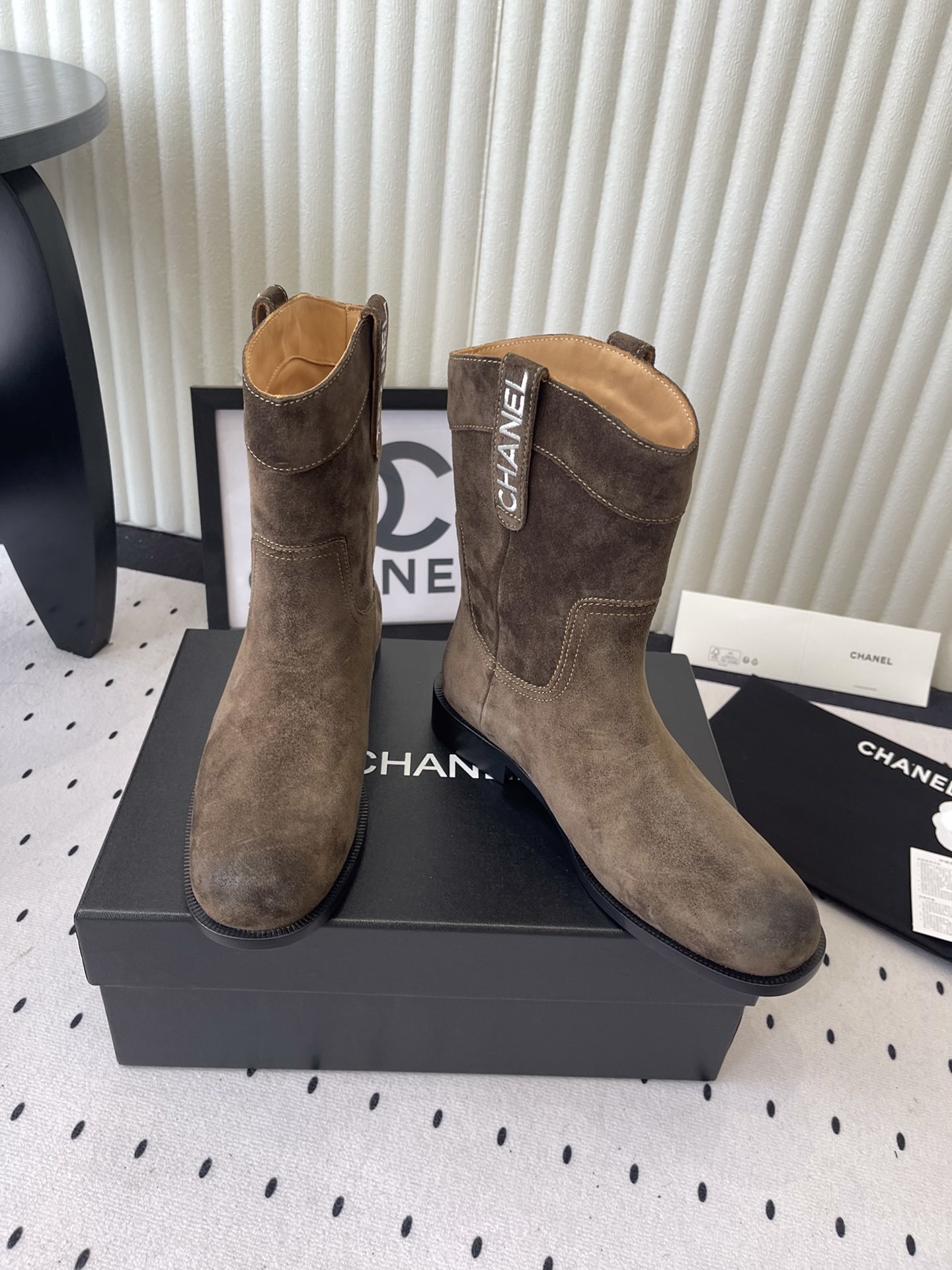 A pair of Chanel brown suede mid-calf Western style boots with embroidered logo pull tabs on a black box. - Hình 7