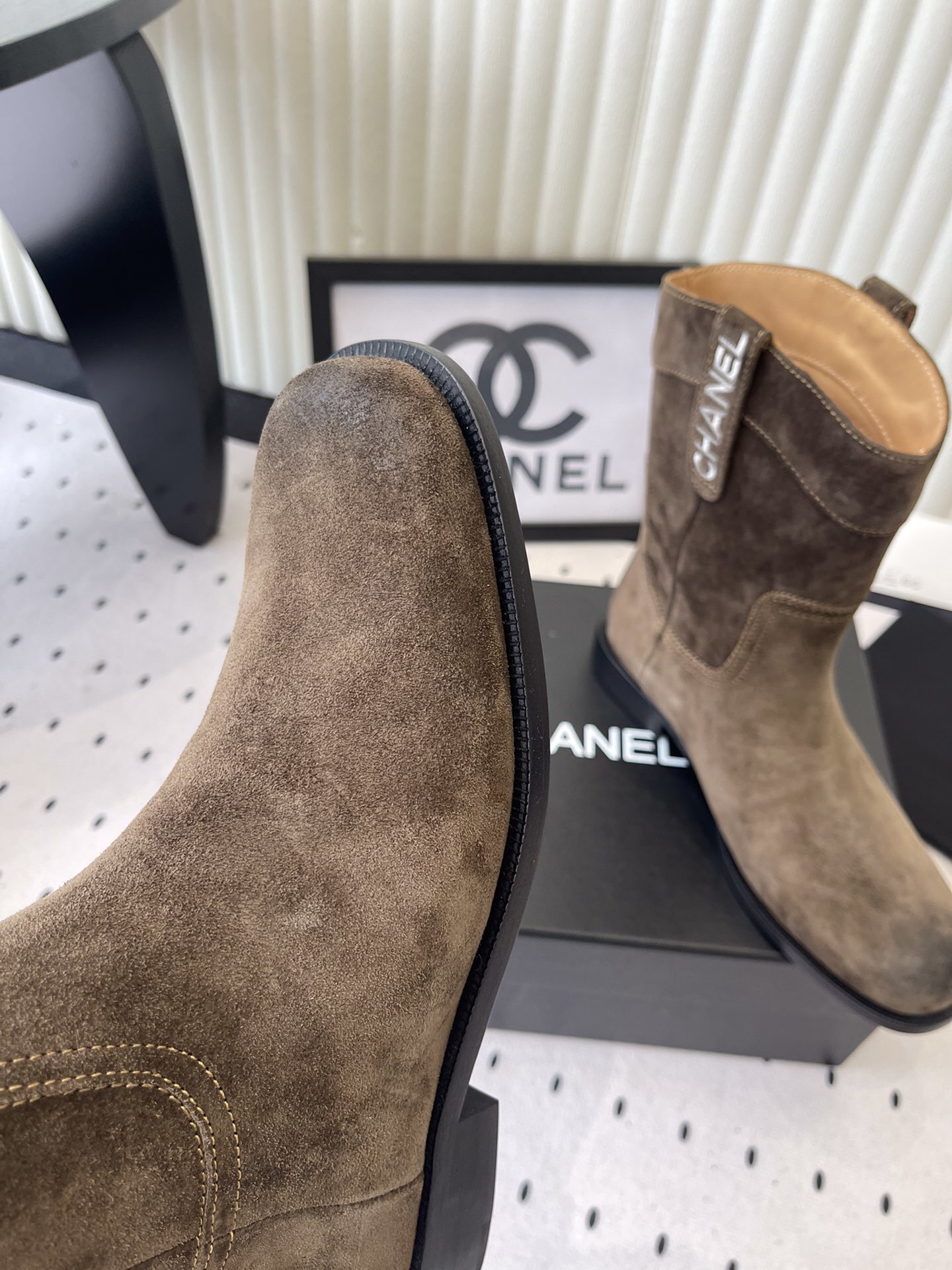 A pair of Chanel brown suede mid-calf Western style boots with embroidered logo pull tabs on a black box. - Hình 6
