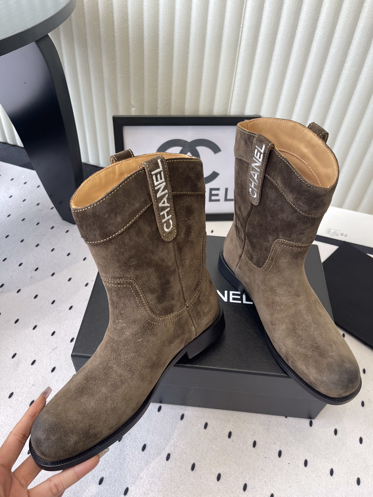 A pair of Chanel brown suede mid-calf Western style boots with embroidered logo pull tabs on a black box. - Hình 5