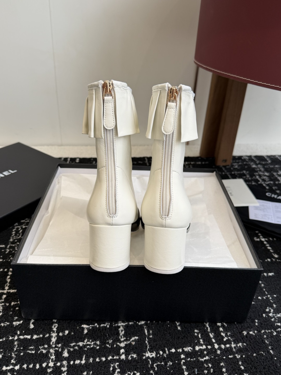A pair of Chanel white leather ankle boots with black patent leather toe caps and ruffled collars on a black designer box. - Hình 8