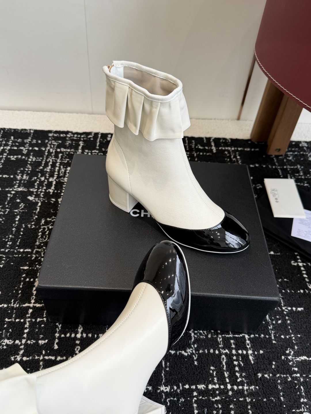 A pair of Chanel white leather ankle boots with black patent leather toe caps and ruffled collars on a black designer box. - Hình 7