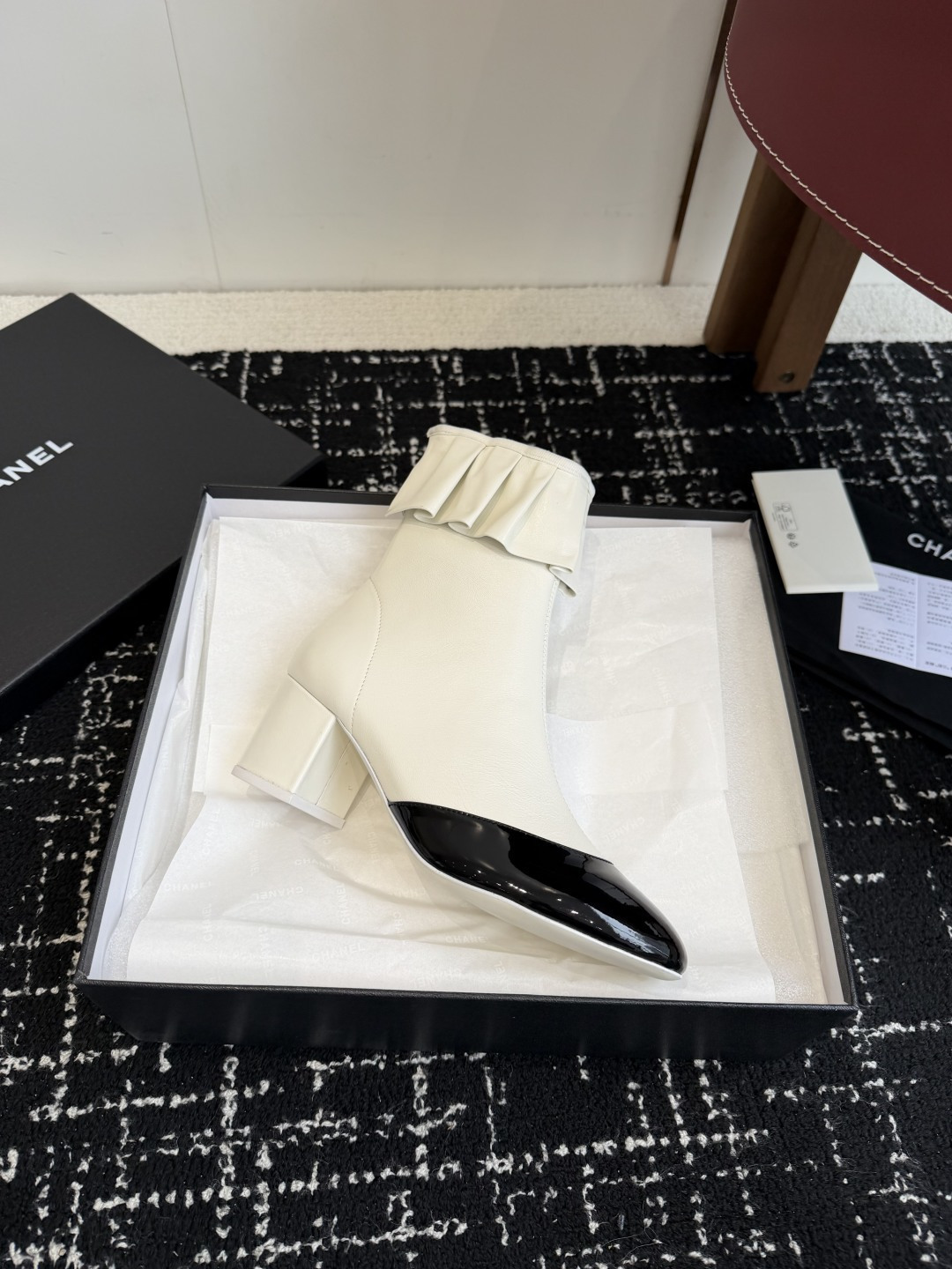 A pair of Chanel white leather ankle boots with black patent leather toe caps and ruffled collars on a black designer box. - Hình 6