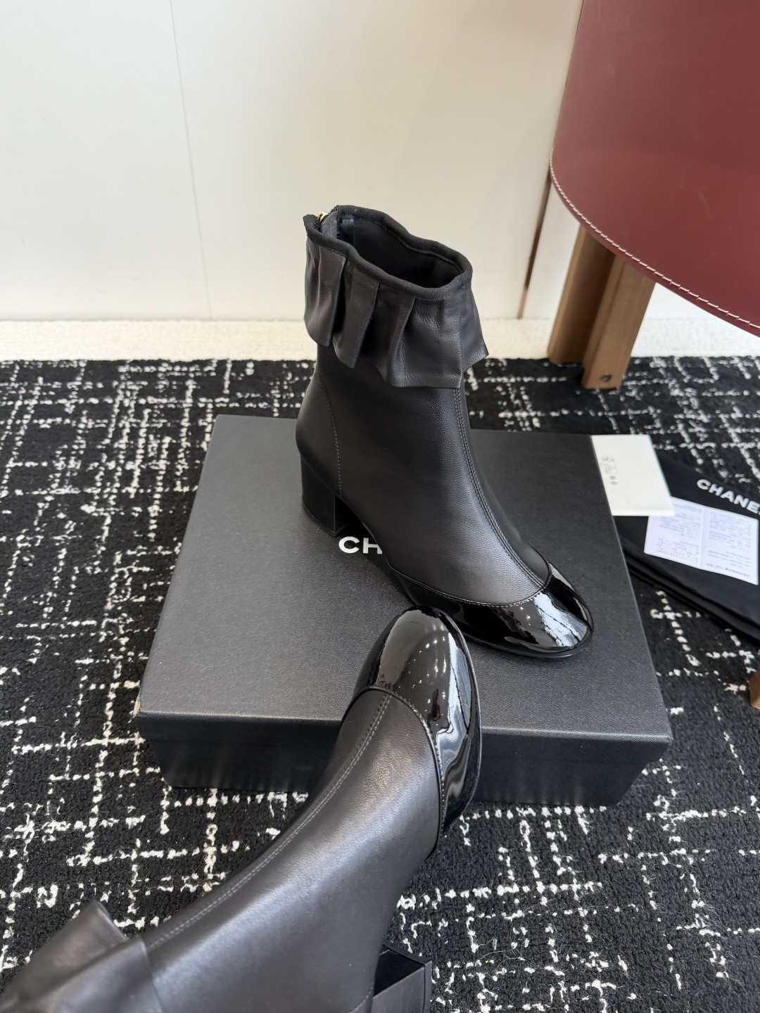 Authentic Chanel black leather ankle boots with ruffle detail and patent toe sitting on a black designer box - Hình 7