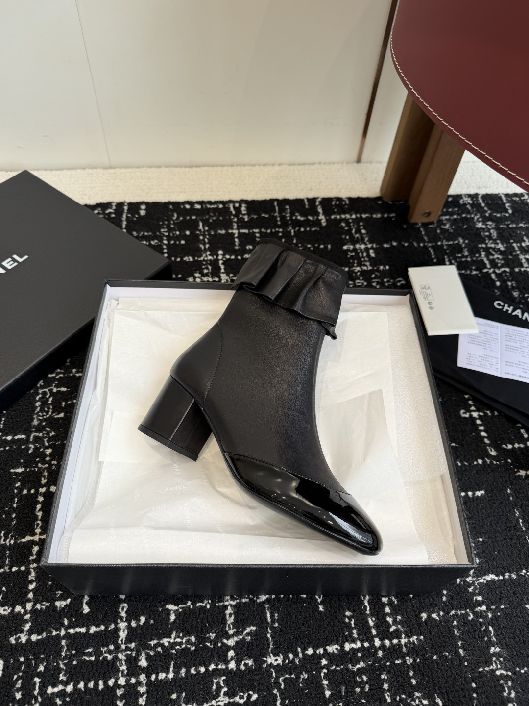 Authentic Chanel black leather ankle boots with ruffle detail and patent toe sitting on a black designer box - Hình 6
