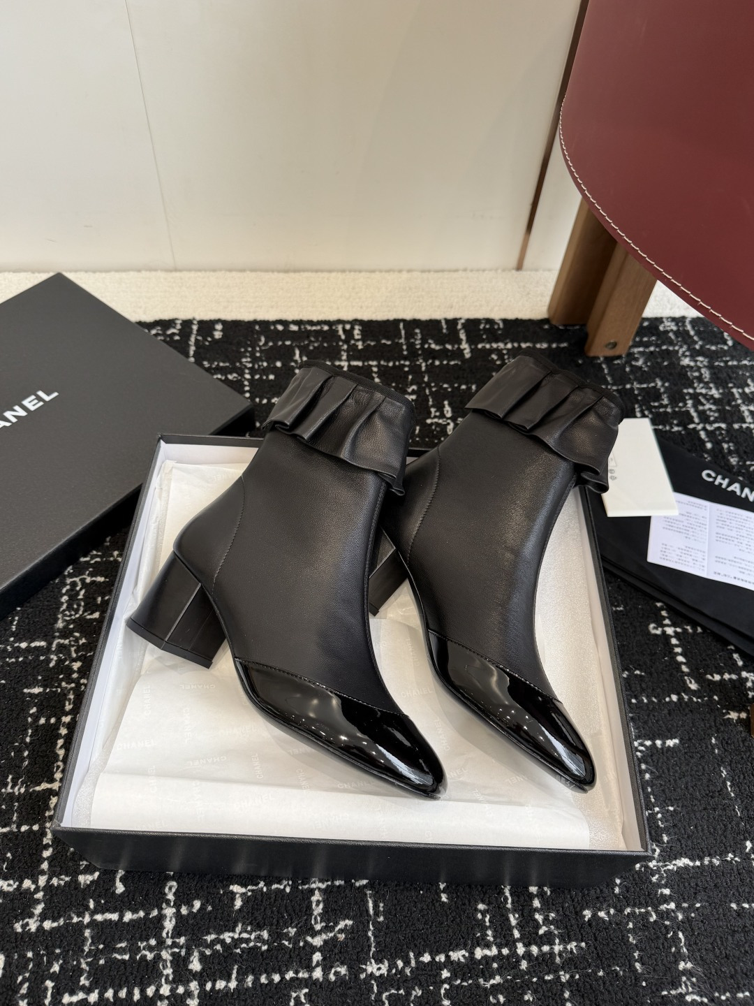 Authentic Chanel black leather ankle boots with ruffle detail and patent toe sitting on a black designer box - Hình 4