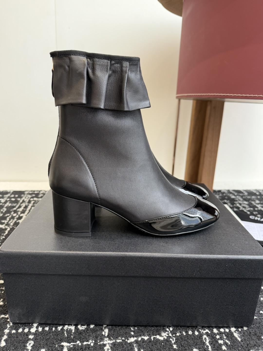 Authentic Chanel black leather ankle boots with ruffle detail and patent toe sitting on a black designer box - Hình 2
