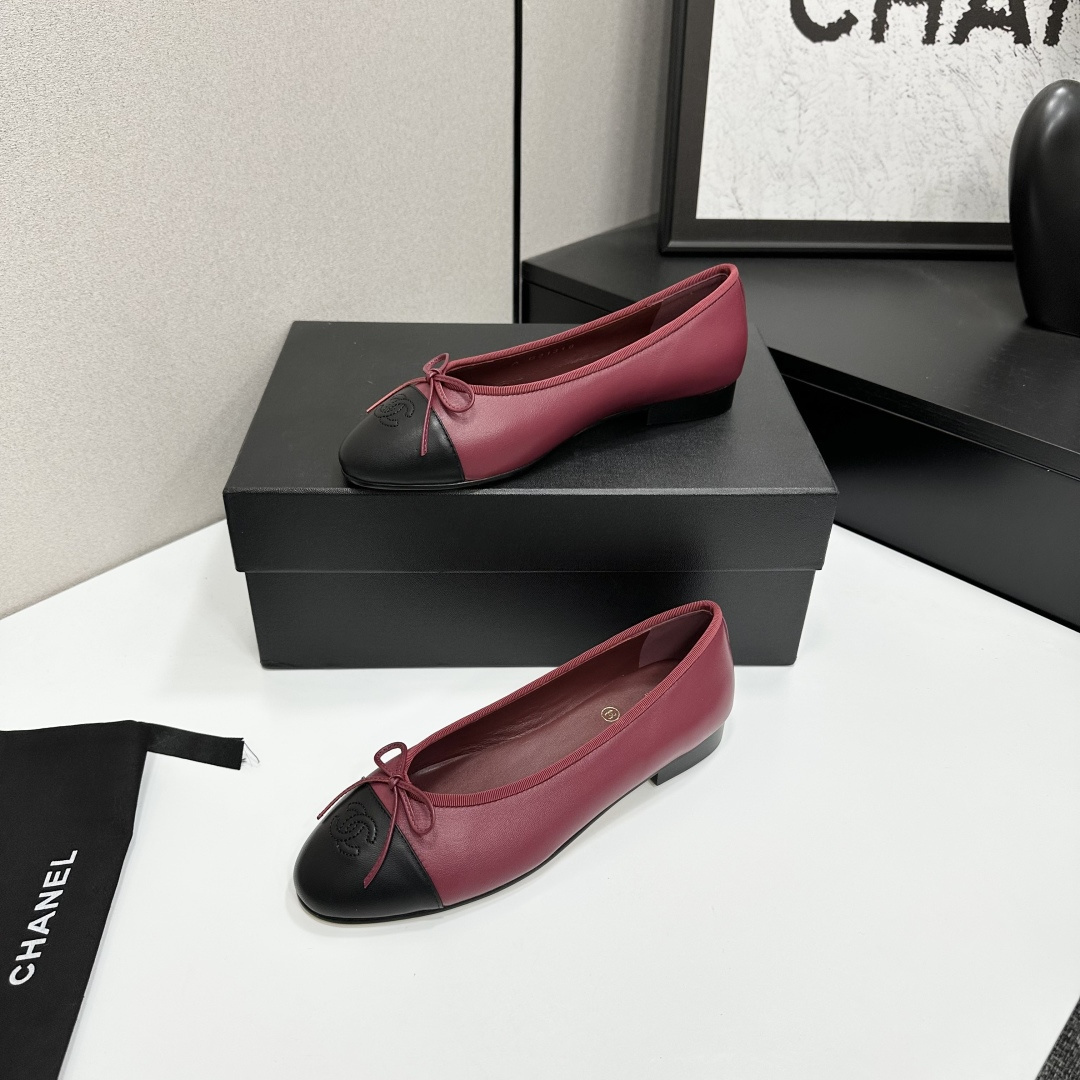 A pair of burgundy leather ballet flats with black cap toes and bow detail resting on a black designer box. - Hình 3