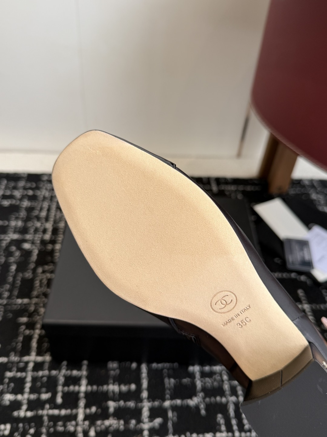 A pair of black Chanel leather ankle boots with glossy patent leather toe caps and block heels featuring the CC logo, displayed on a black box. - Hình 9