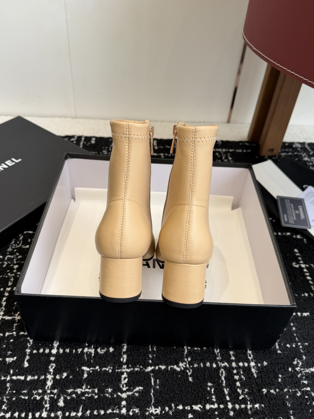 A pair of Chanel two-tone beige leather ankle boots with black fabric cap-toes and gold CC logo on the block heels, presented on a black Chanel box. - Hình 8