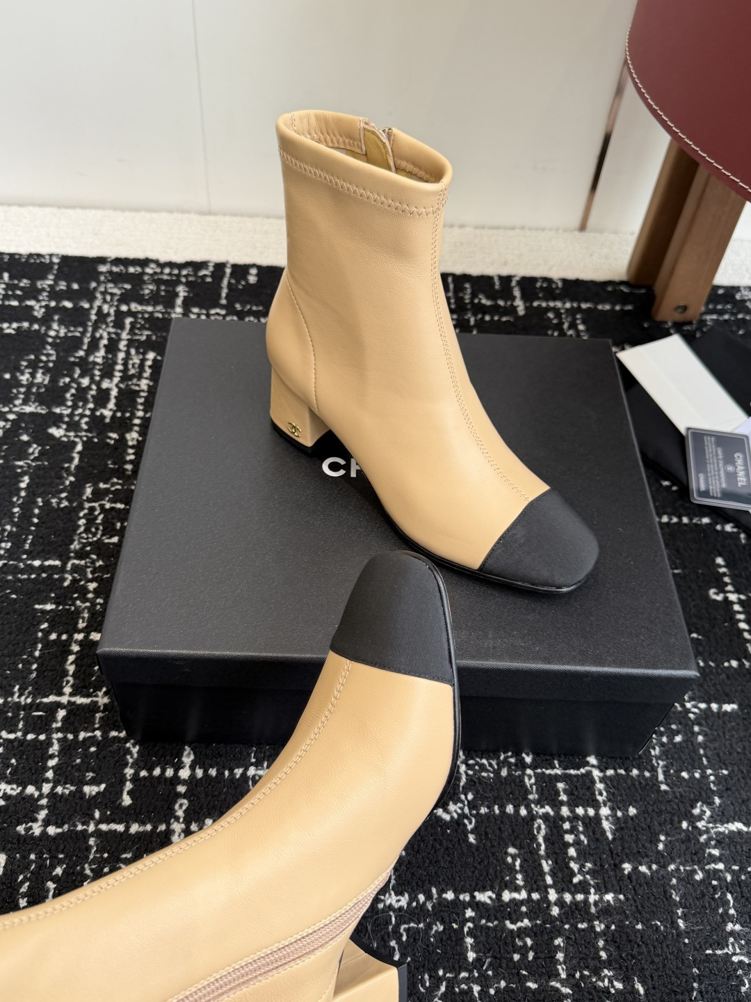 A pair of Chanel two-tone beige leather ankle boots with black fabric cap-toes and gold CC logo on the block heels, presented on a black Chanel box. - Hình 7