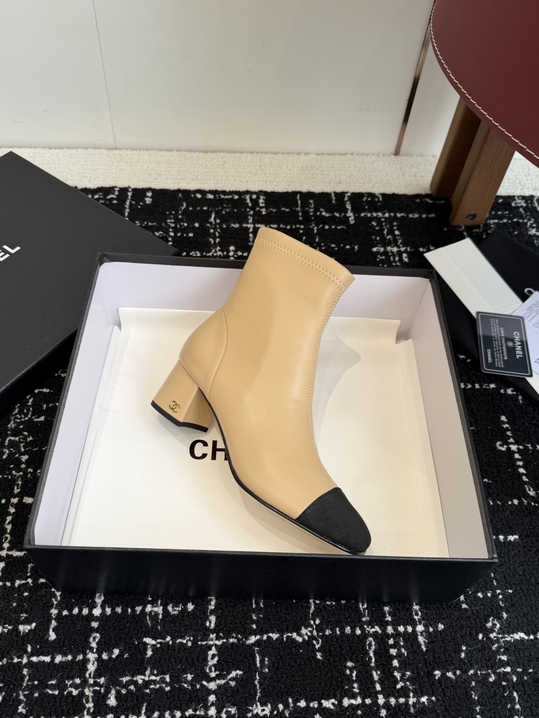 A pair of Chanel two-tone beige leather ankle boots with black fabric cap-toes and gold CC logo on the block heels, presented on a black Chanel box. - Hình 6
