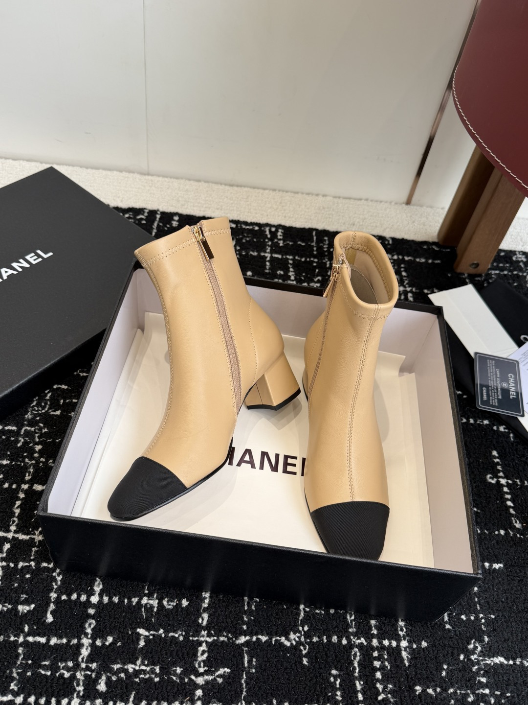 A pair of Chanel two-tone beige leather ankle boots with black fabric cap-toes and gold CC logo on the block heels, presented on a black Chanel box. - Hình 5