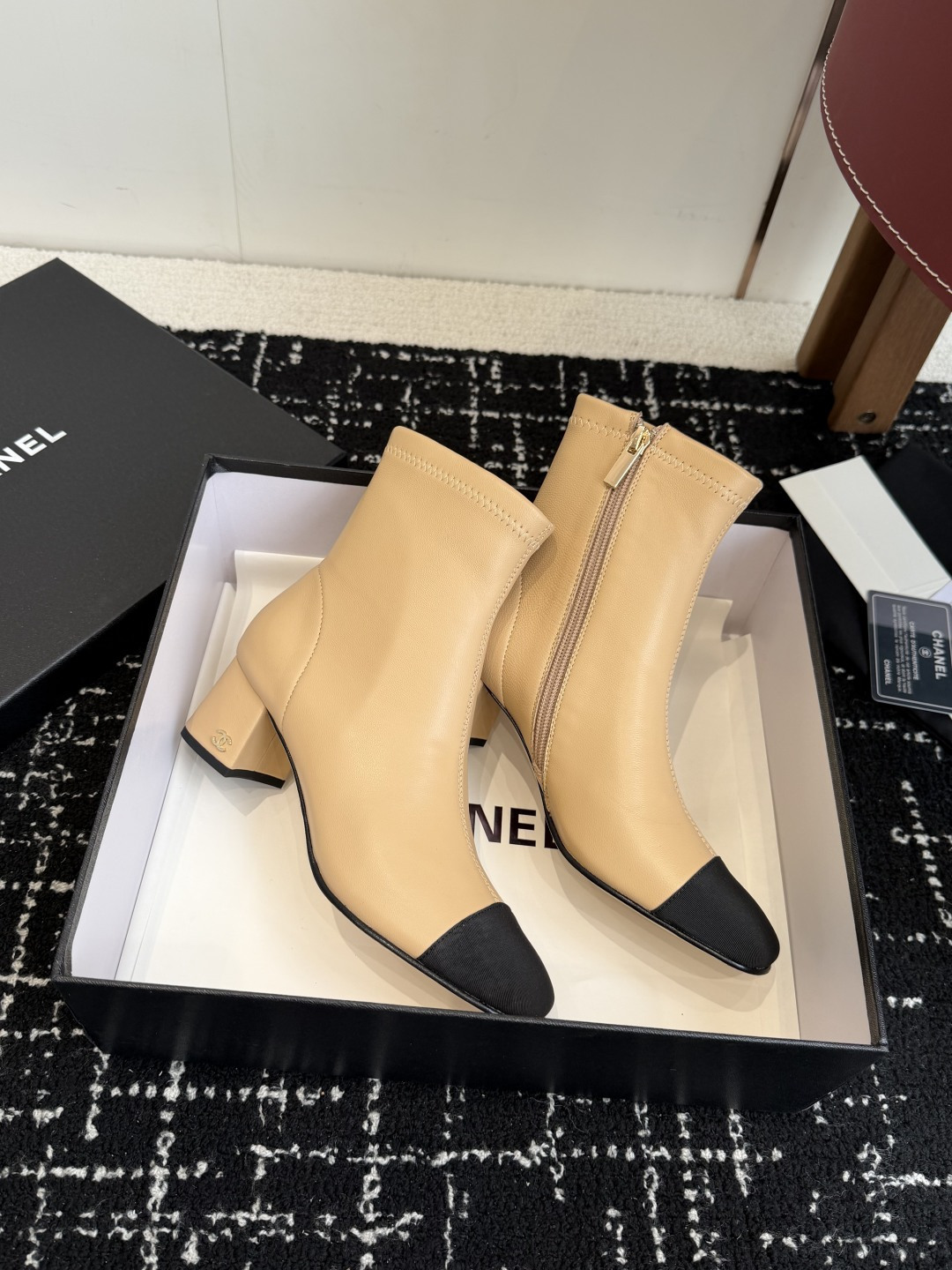 A pair of Chanel two-tone beige leather ankle boots with black fabric cap-toes and gold CC logo on the block heels, presented on a black Chanel box. - Hình 4