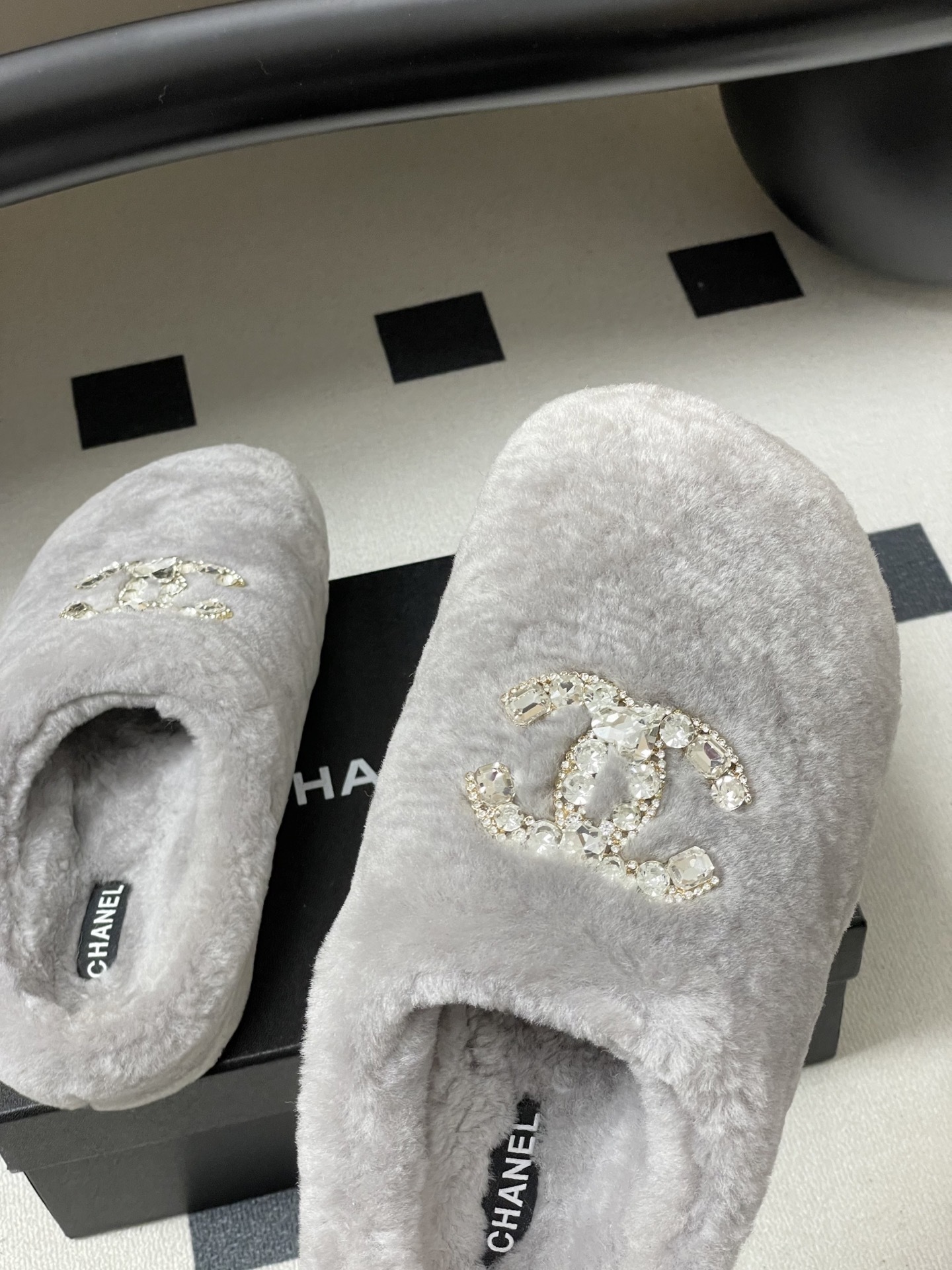 A pair of grey plush faux fur slippers with a sparkling rhinestone crystal logo on a black surface. - Hình 9