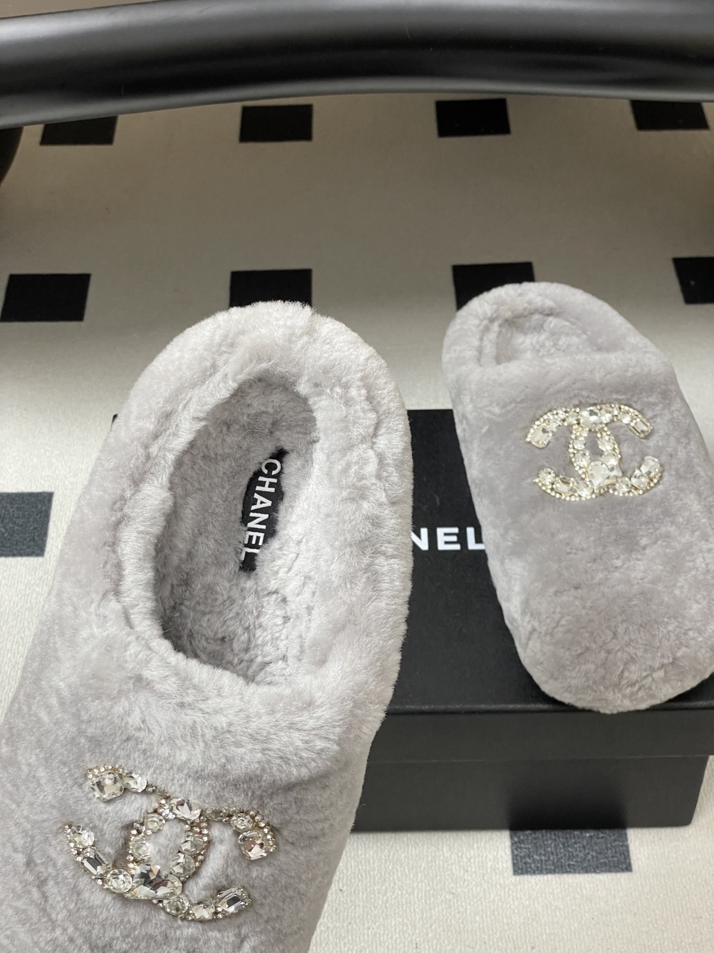 A pair of grey plush faux fur slippers with a sparkling rhinestone crystal logo on a black surface. - Hình 7
