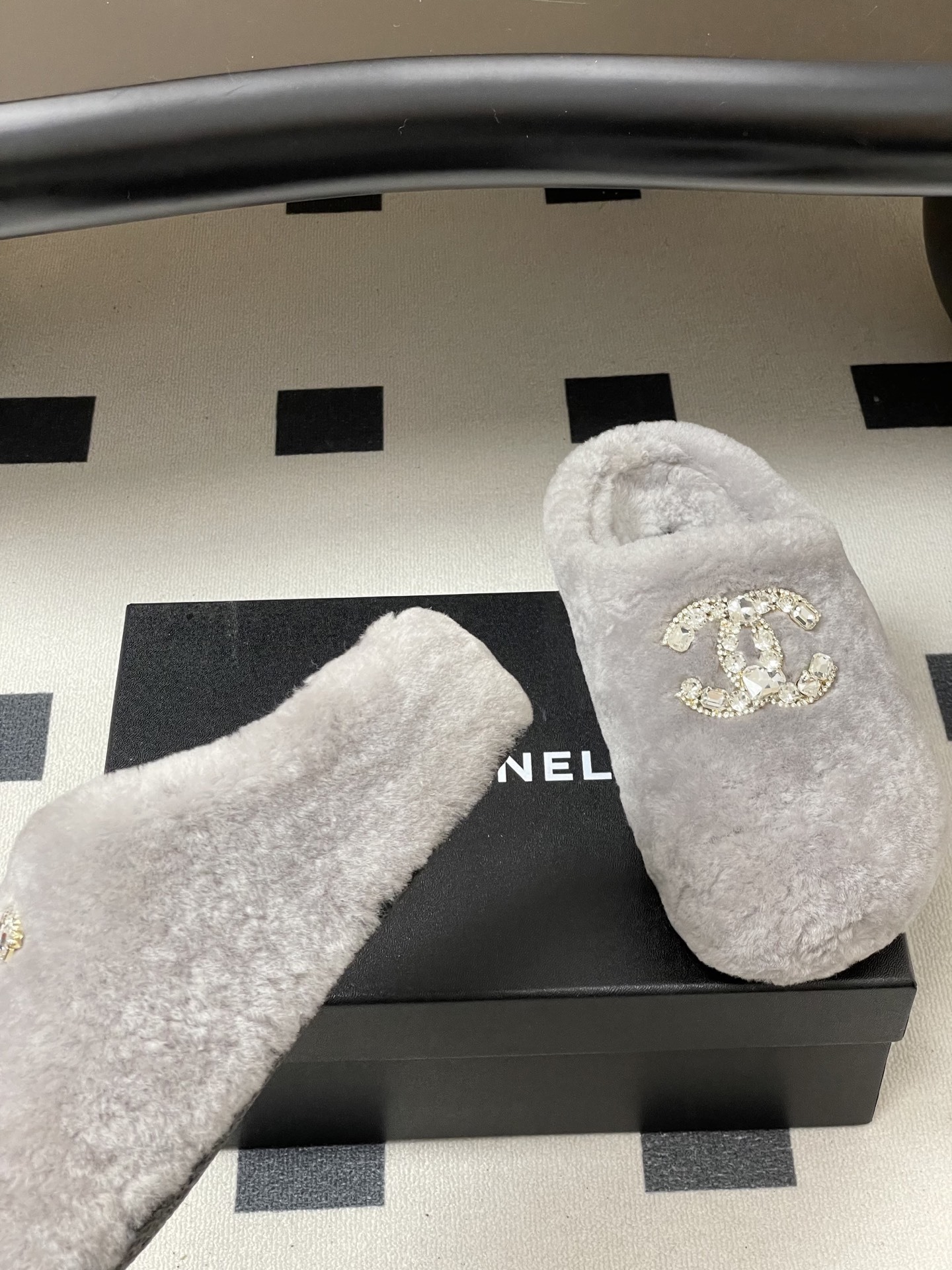A pair of grey plush faux fur slippers with a sparkling rhinestone crystal logo on a black surface. - Hình 6
