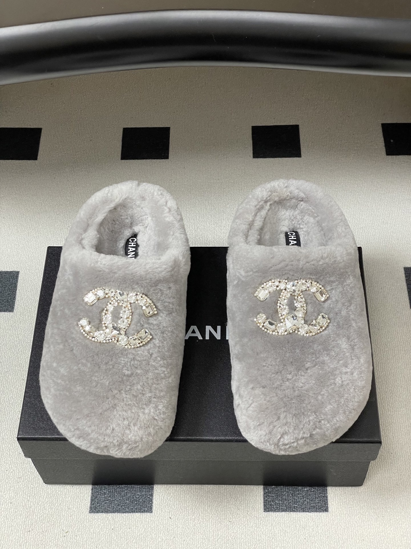 A pair of grey plush faux fur slippers with a sparkling rhinestone crystal logo on a black surface. - Hình 5