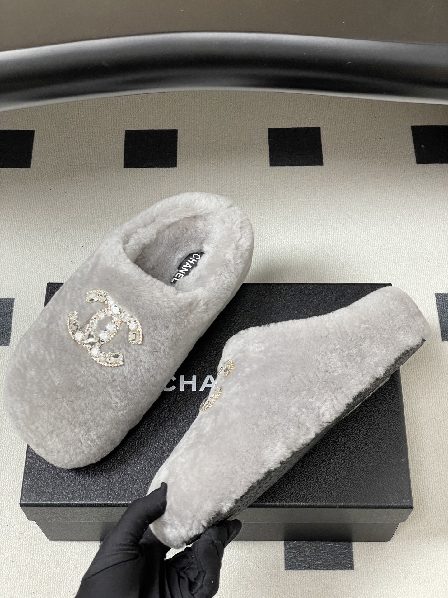 A pair of grey plush faux fur slippers with a sparkling rhinestone crystal logo on a black surface. - Hình 4