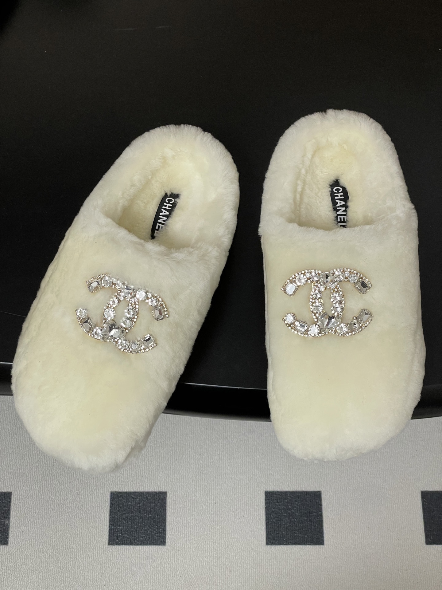 A pair of plush white faux fur slippers featuring a large sparkling crystal encrusted double-C logo on the top. - Hình 2