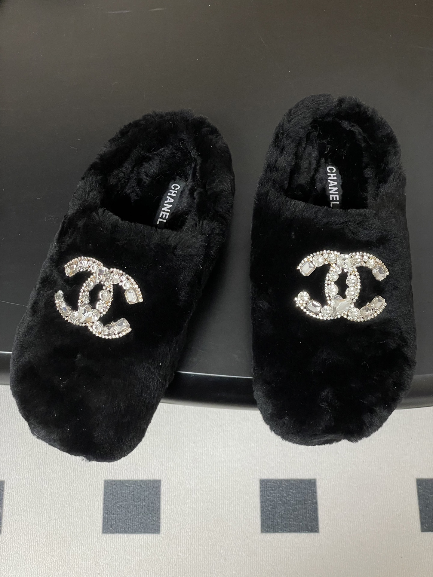 Elegant black fluffy slippers featuring a prominent crystal-studded double-C logo design on a black surface. - Hình 2