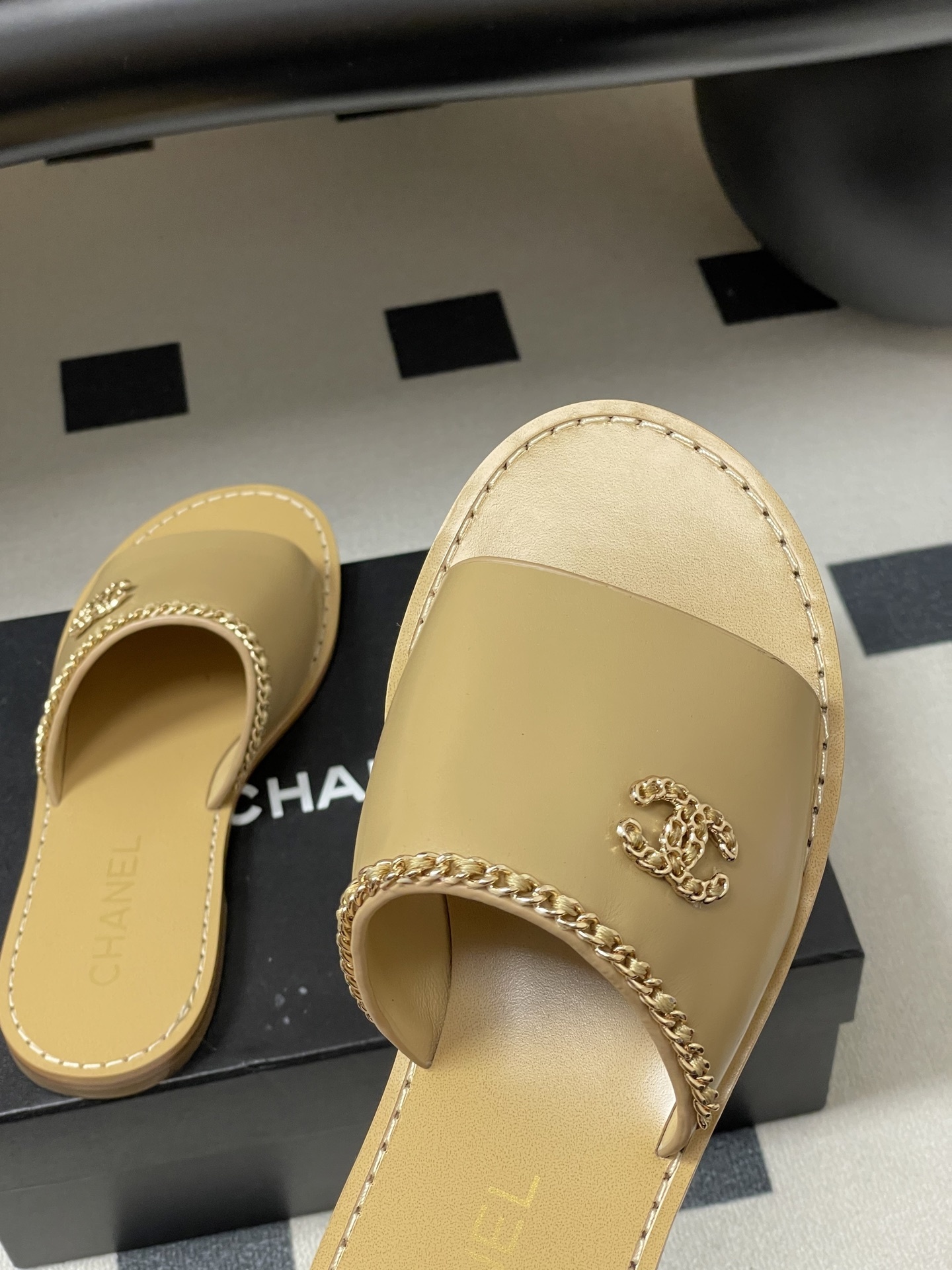 Luxury beige Chanel leather flat sandals with gold chain trim and interlocking CC logo on a black surface. - Hình 9