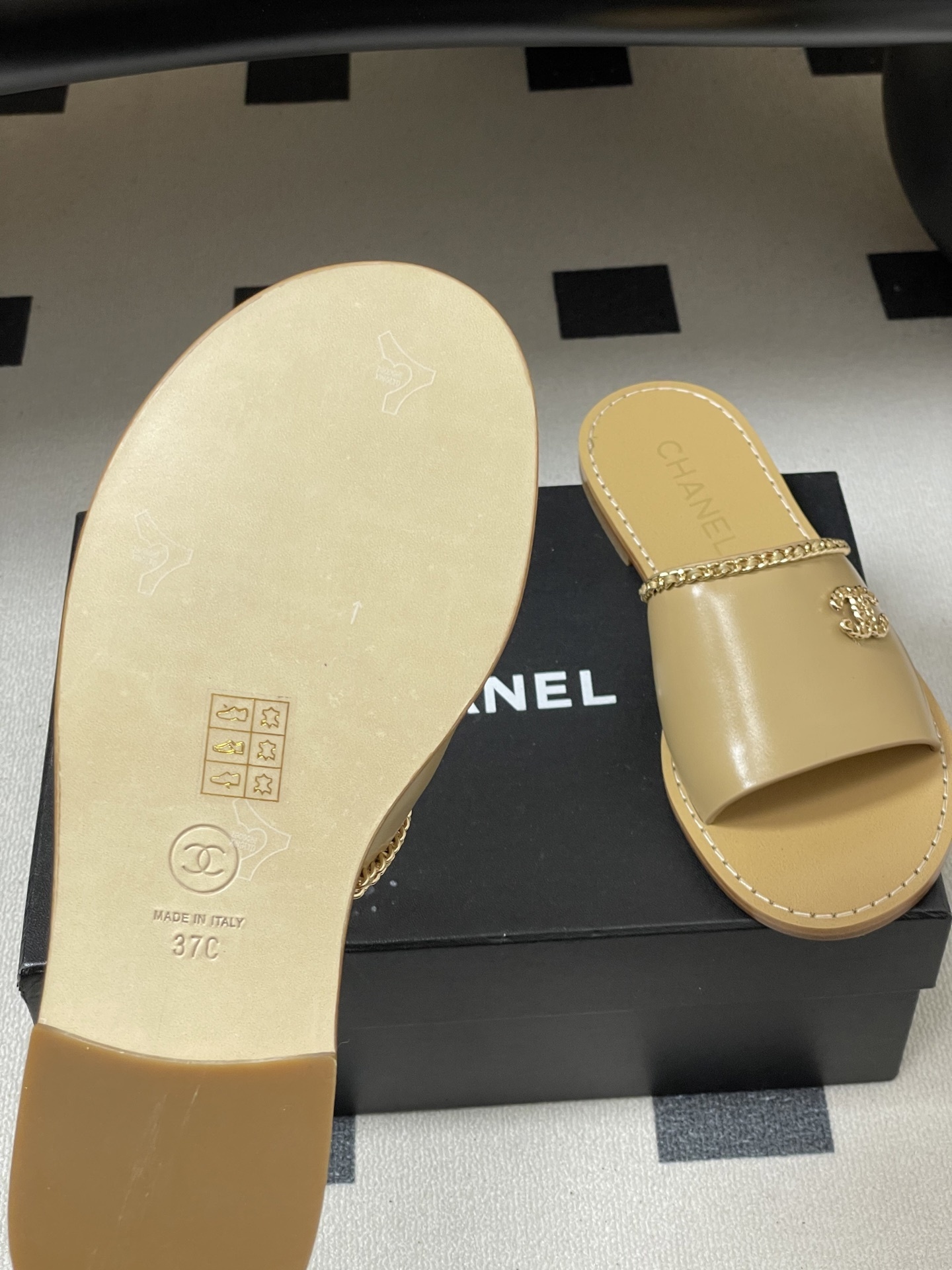 Luxury beige Chanel leather flat sandals with gold chain trim and interlocking CC logo on a black surface. - Hình 8