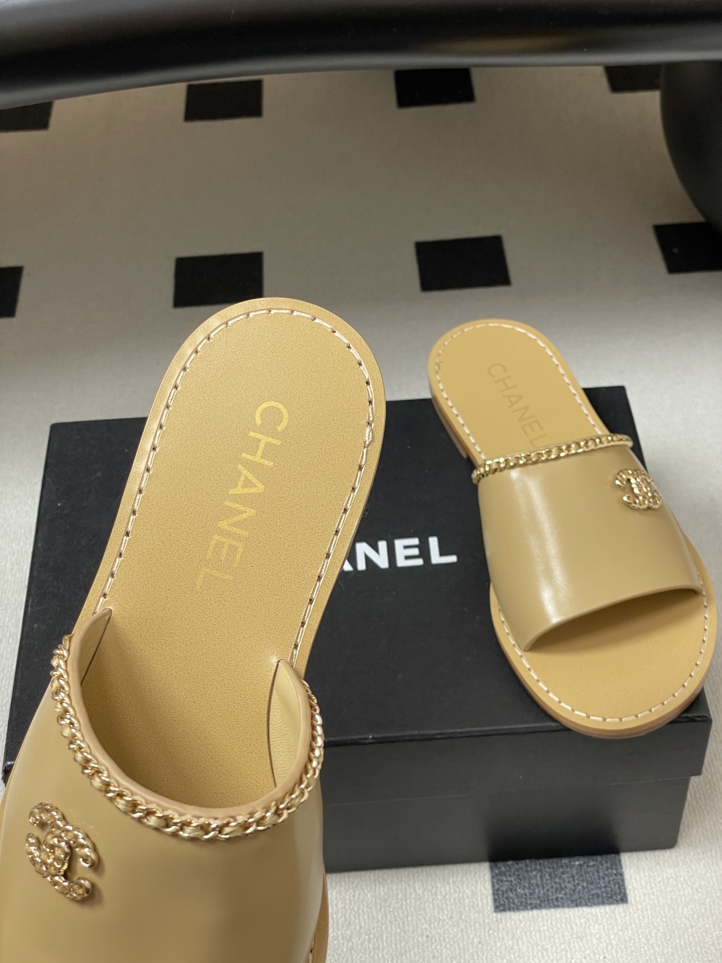 Luxury beige Chanel leather flat sandals with gold chain trim and interlocking CC logo on a black surface. - Hình 7