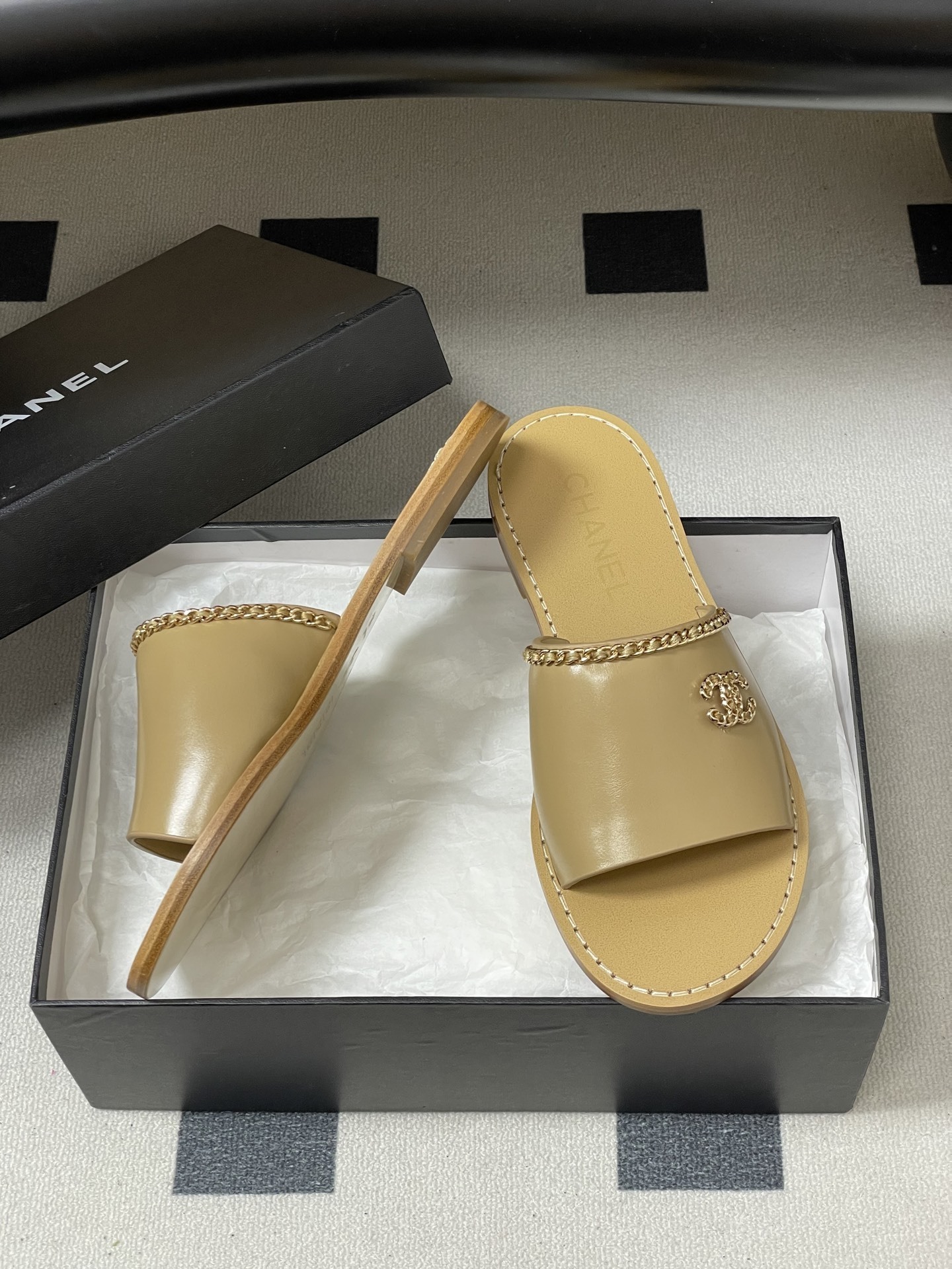 Luxury beige Chanel leather flat sandals with gold chain trim and interlocking CC logo on a black surface. - Hình 6