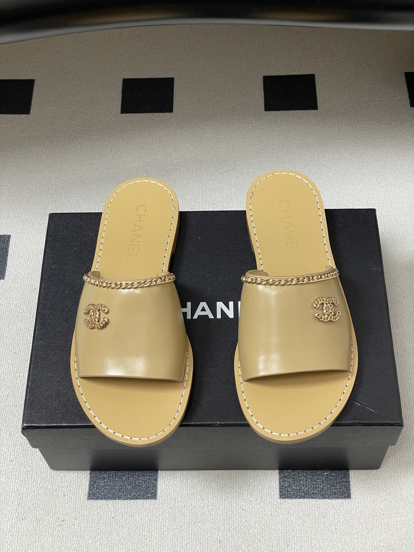 Luxury beige Chanel leather flat sandals with gold chain trim and interlocking CC logo on a black surface. - Hình 5