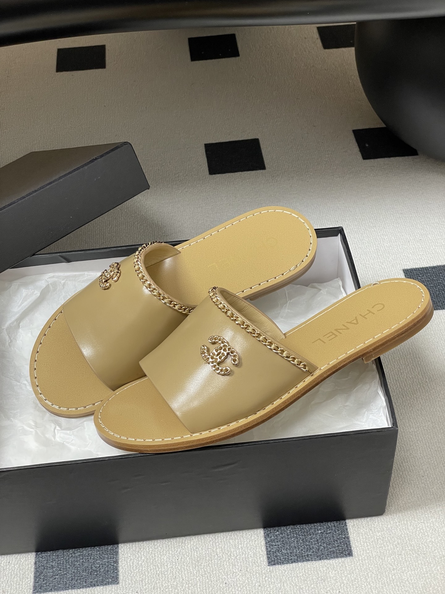 Luxury beige Chanel leather flat sandals with gold chain trim and interlocking CC logo on a black surface. - Hình 4