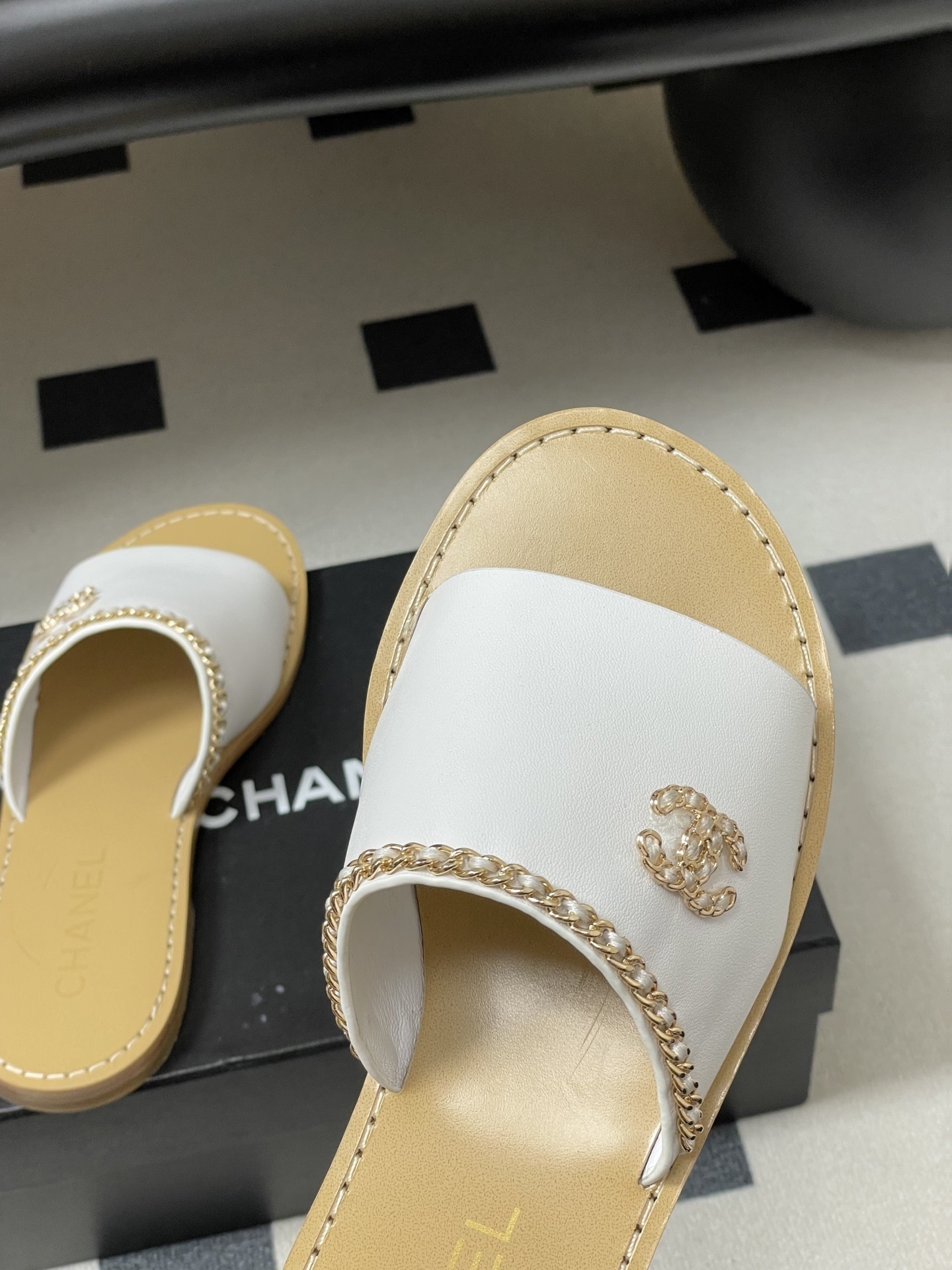 Pair of Chanel white leather flat sandals with gold chain detail and crystal embellished CC logo on a black surface. - Hình 9
