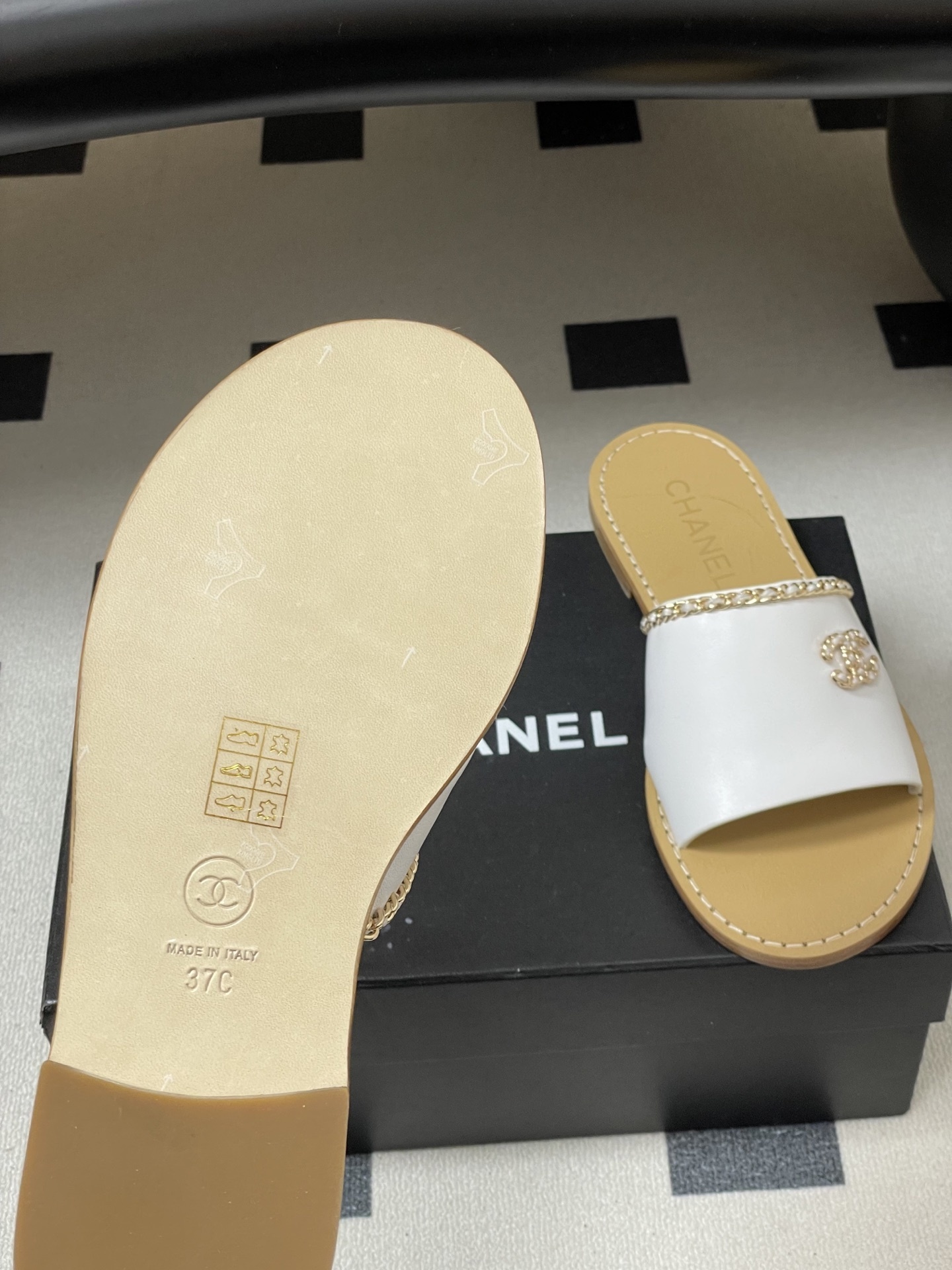 Pair of Chanel white leather flat sandals with gold chain detail and crystal embellished CC logo on a black surface. - Hình 8