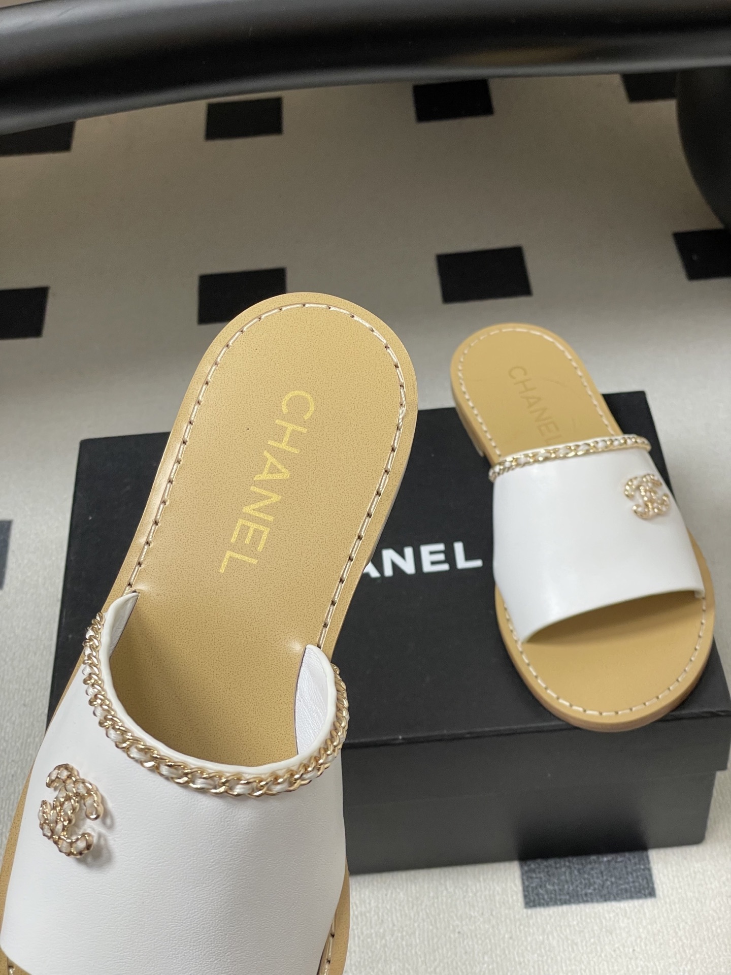Pair of Chanel white leather flat sandals with gold chain detail and crystal embellished CC logo on a black surface. - Hình 7