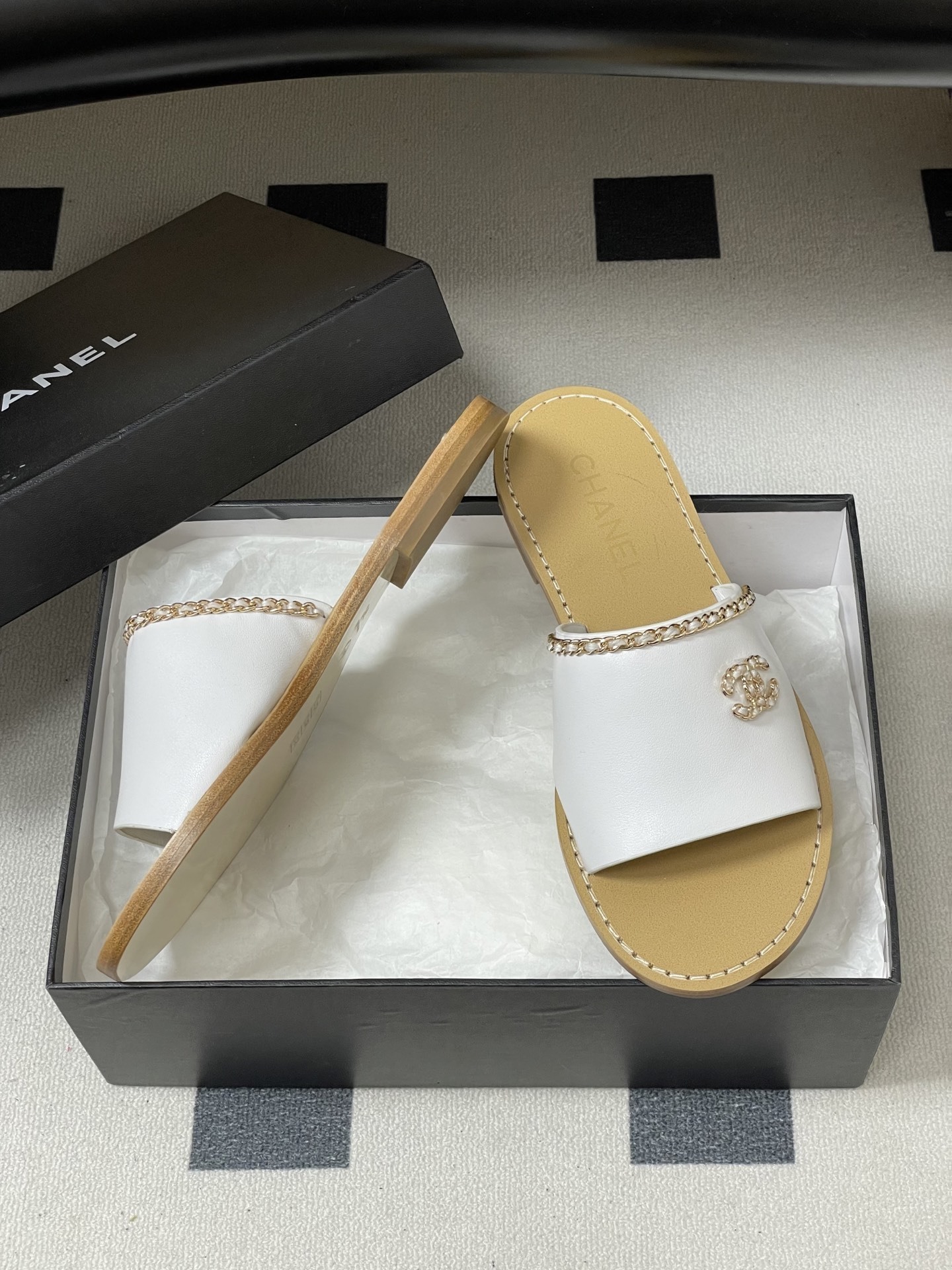 Pair of Chanel white leather flat sandals with gold chain detail and crystal embellished CC logo on a black surface. - Hình 6