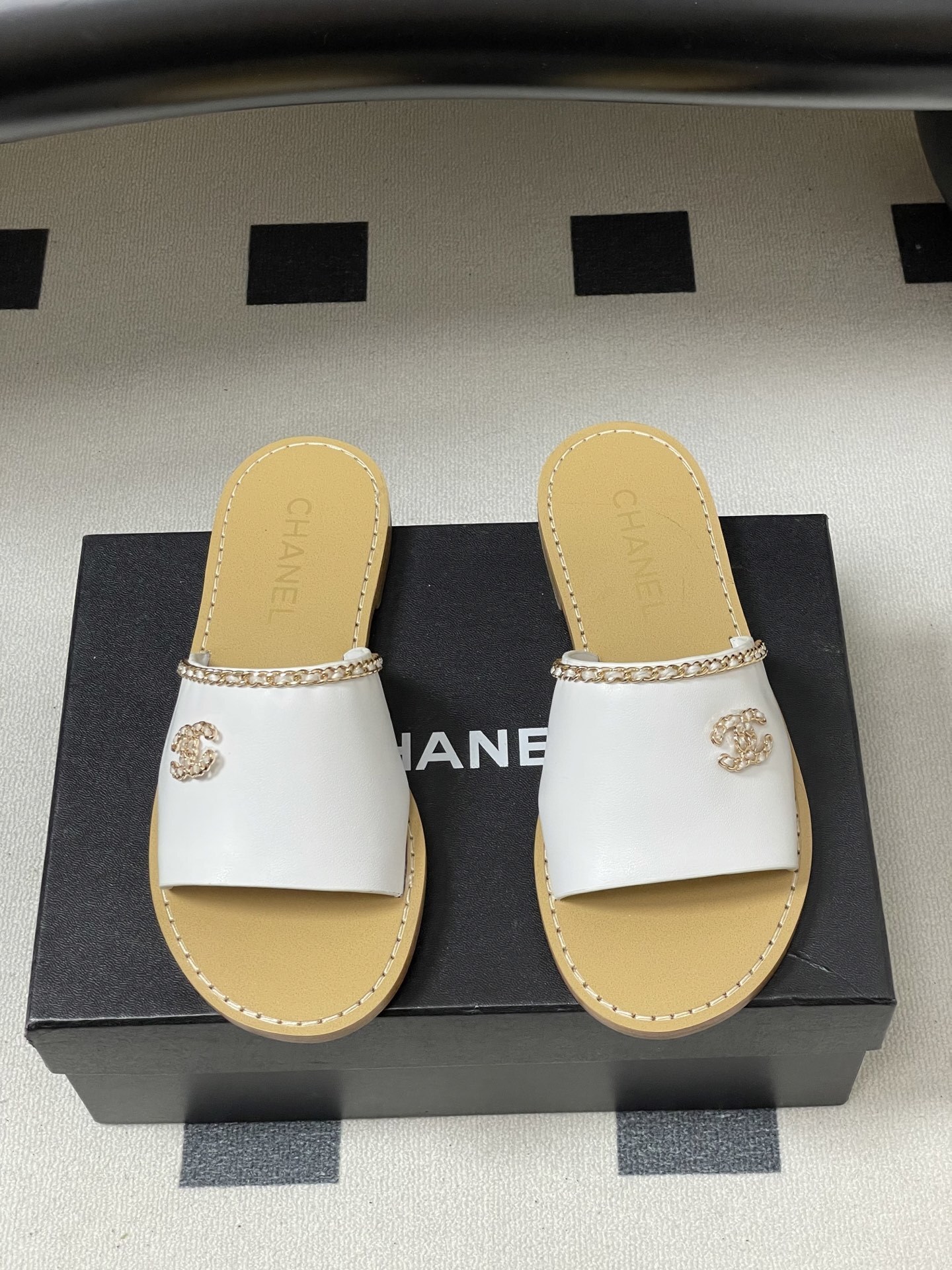 Pair of Chanel white leather flat sandals with gold chain detail and crystal embellished CC logo on a black surface. - Hình 5
