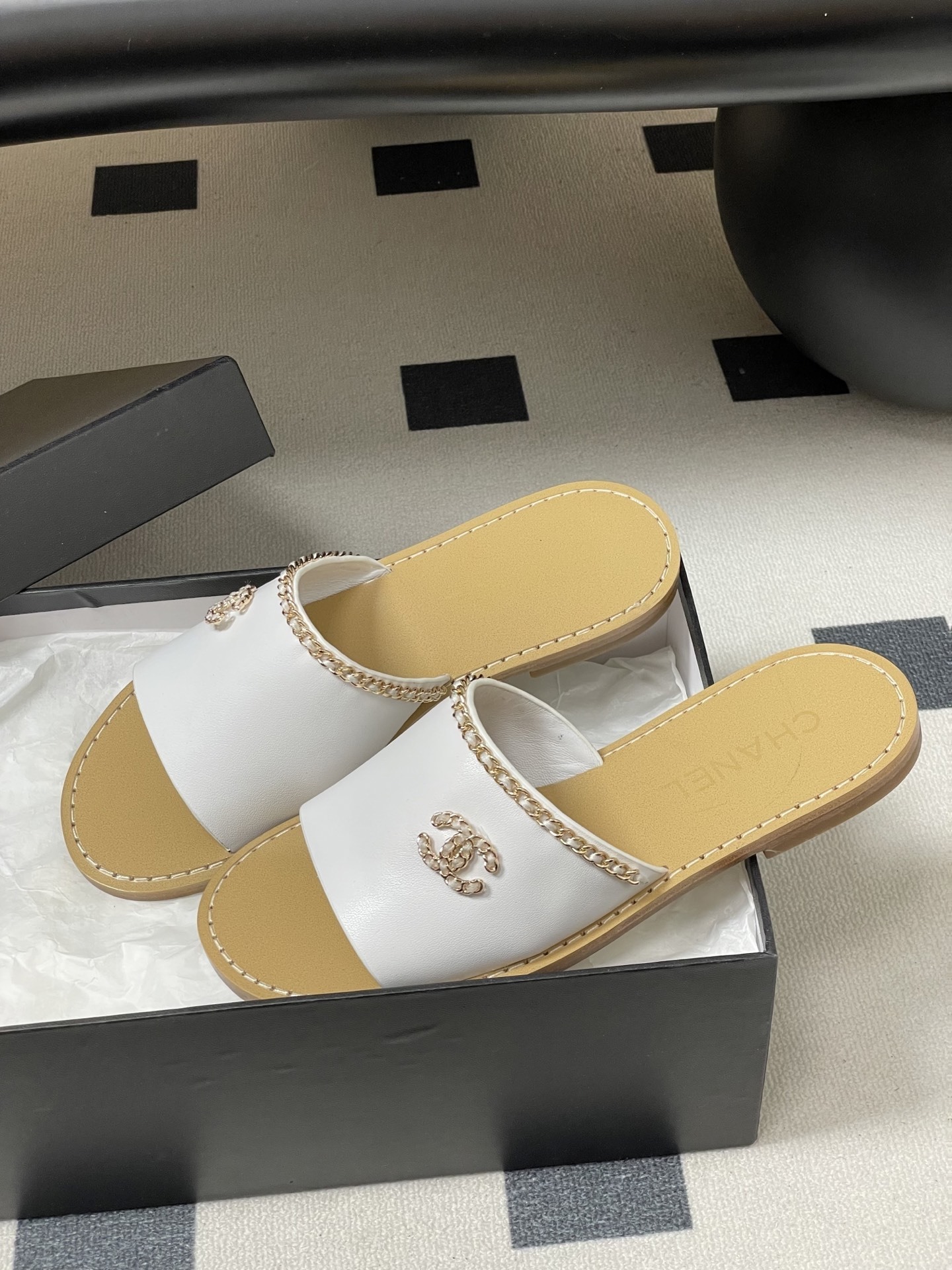 Pair of Chanel white leather flat sandals with gold chain detail and crystal embellished CC logo on a black surface. - Hình 4