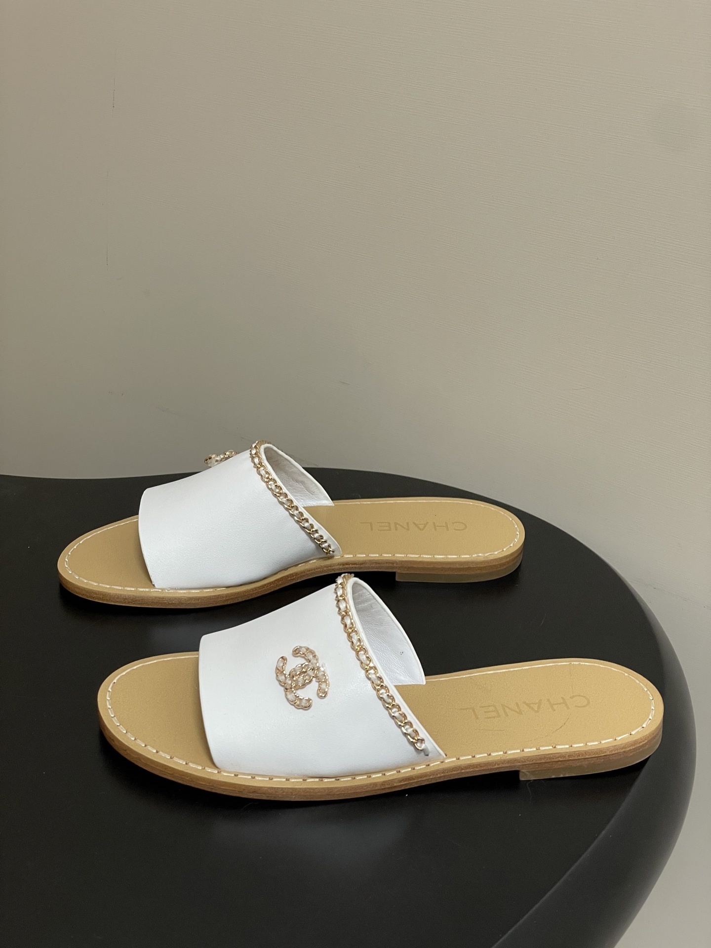 Pair of Chanel white leather flat sandals with gold chain detail and crystal embellished CC logo on a black surface. - Hình 3