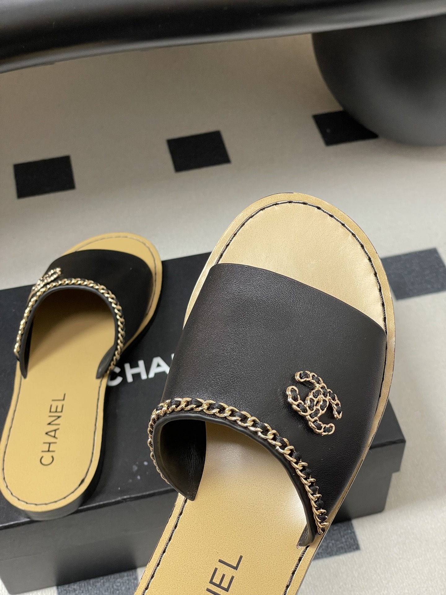 Pair of Chanel black leather flat sandals with gold chain trim and interlocking CC logo on a black surface - Hình 9