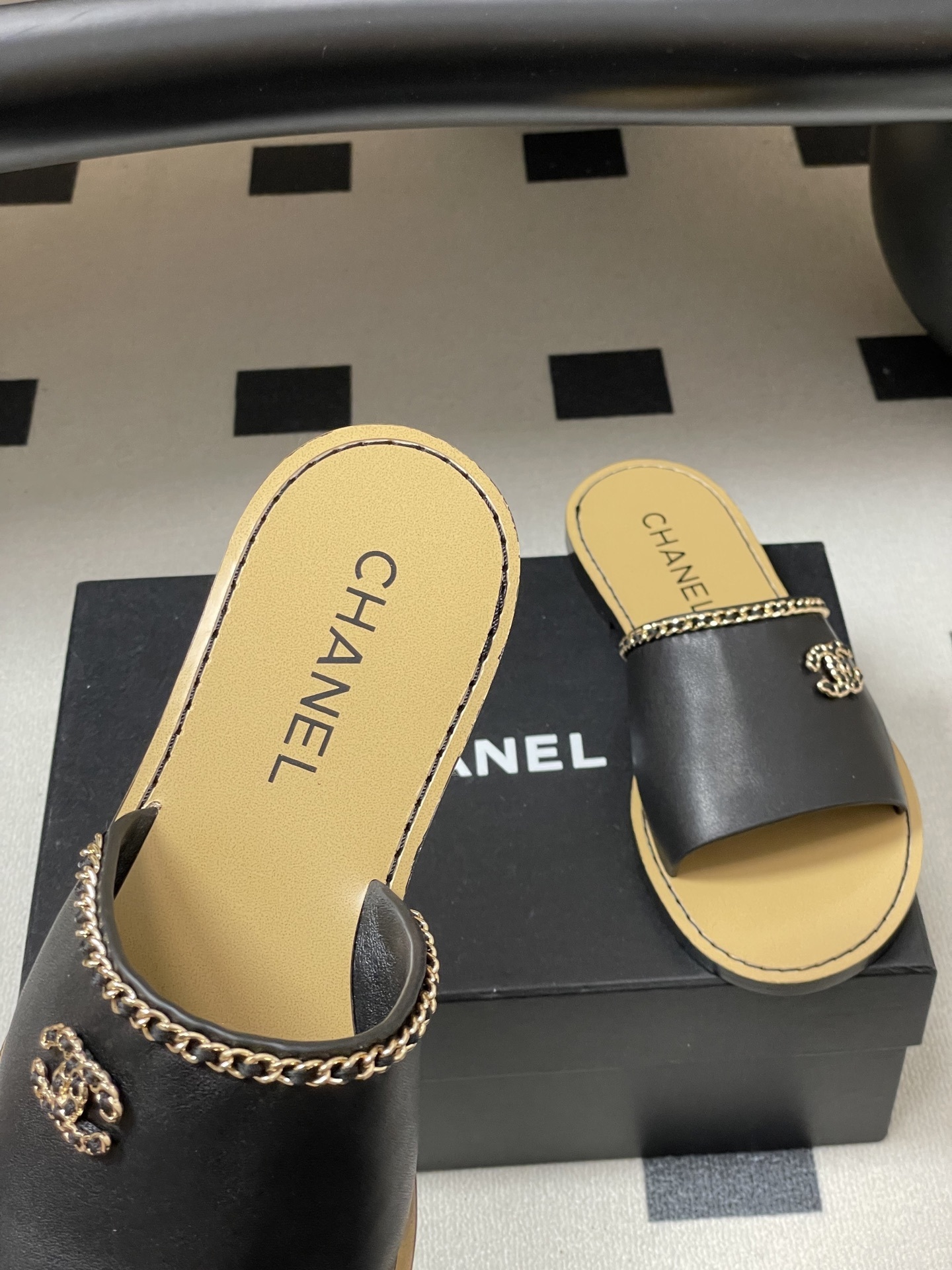 Pair of Chanel black leather flat sandals with gold chain trim and interlocking CC logo on a black surface - Hình 7