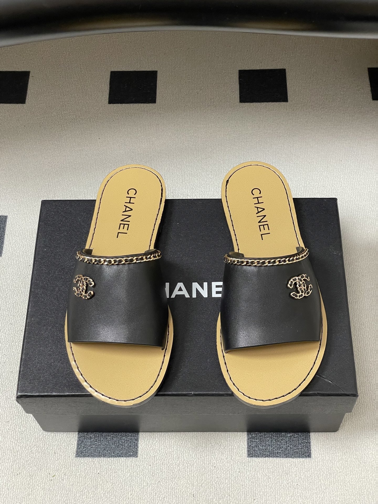 Pair of Chanel black leather flat sandals with gold chain trim and interlocking CC logo on a black surface - Hình 5