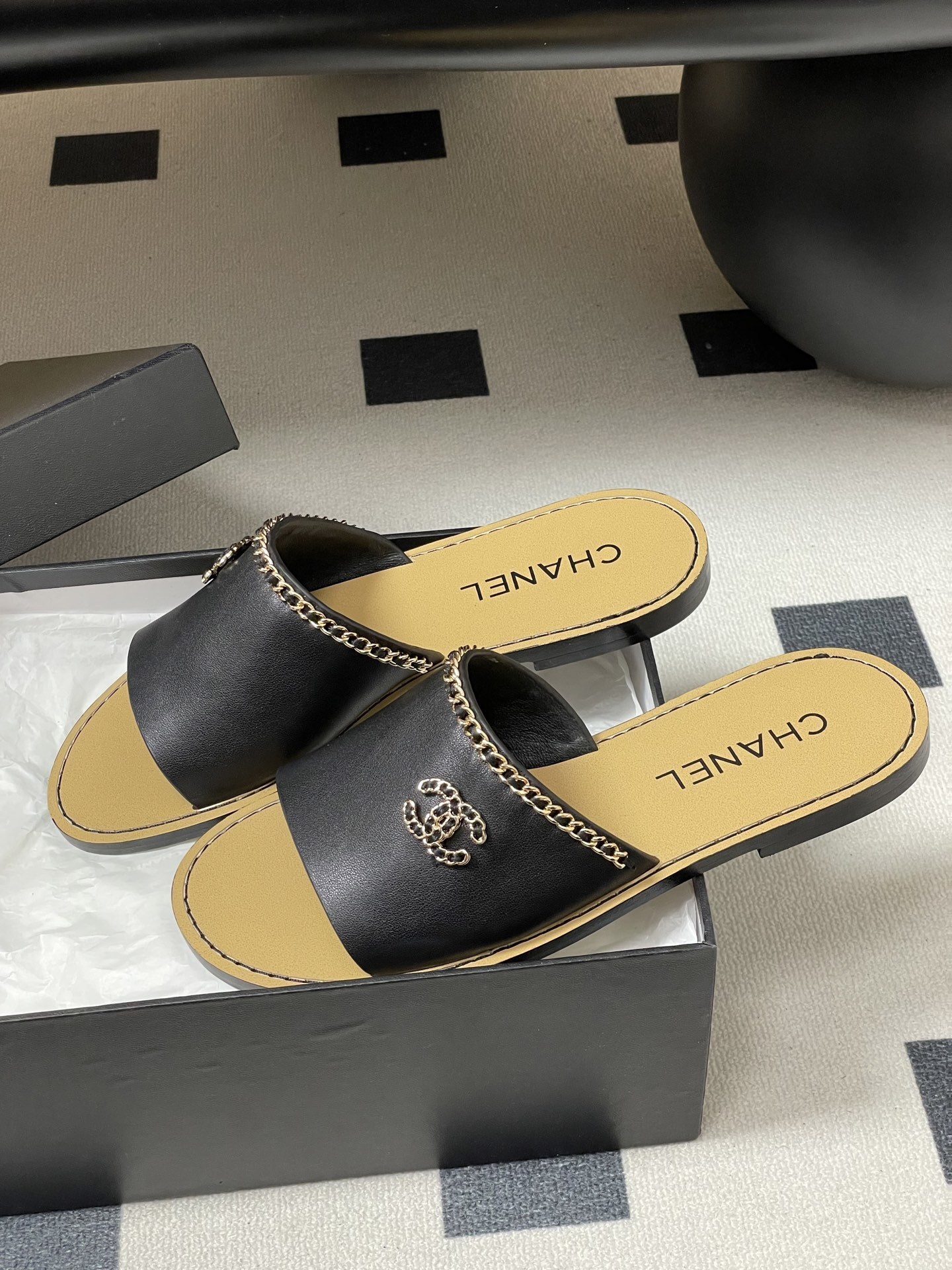 Pair of Chanel black leather flat sandals with gold chain trim and interlocking CC logo on a black surface - Hình 4