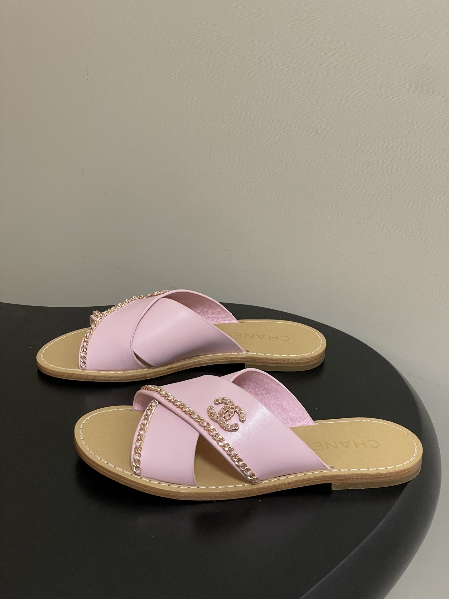 Pair of Chanel light pink leather criss-cross sandals with gold chain detail and CC logo on a black surface - Hình 3