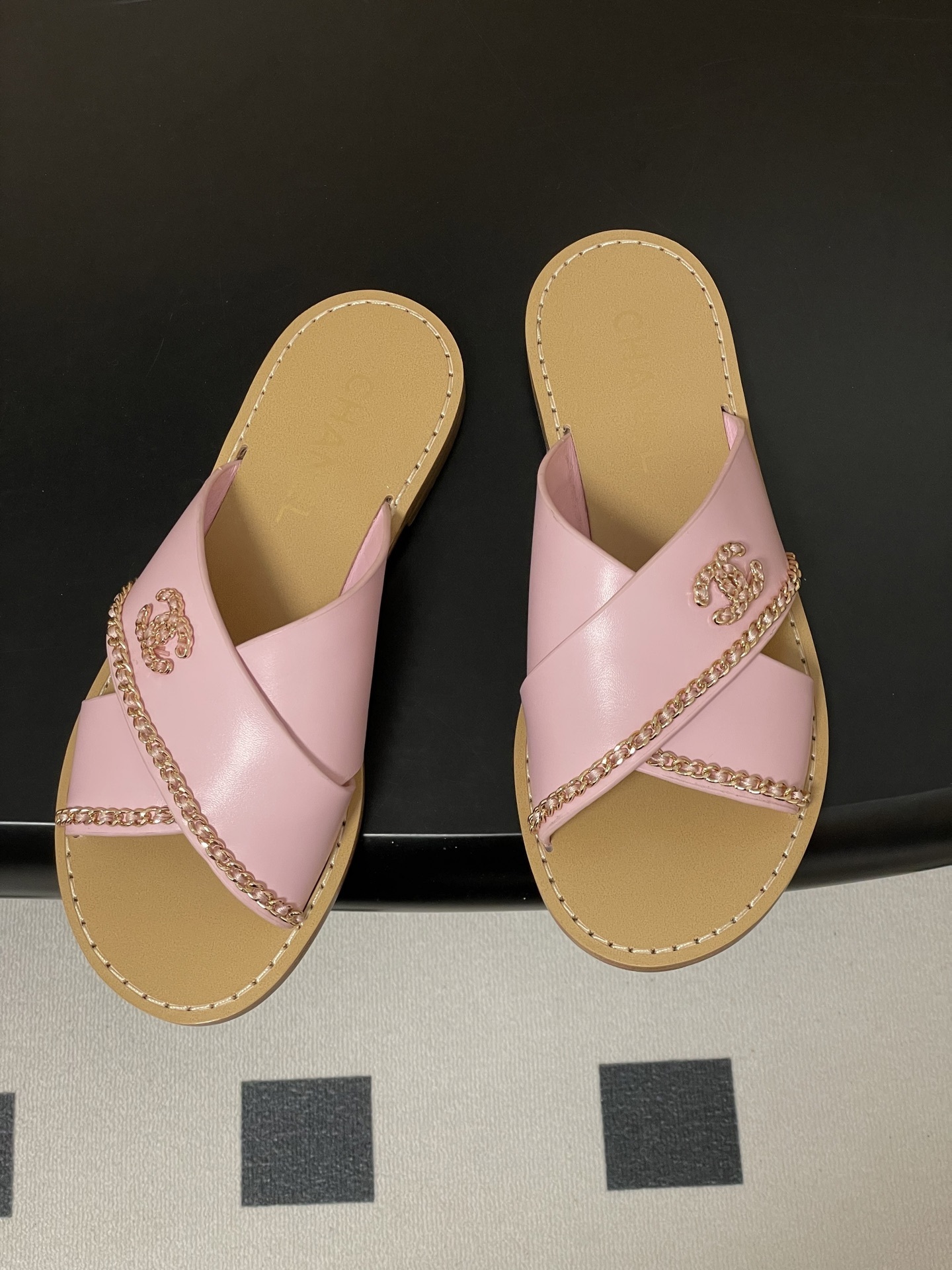 Pair of Chanel light pink leather criss-cross sandals with gold chain detail and CC logo on a black surface - Hình 2