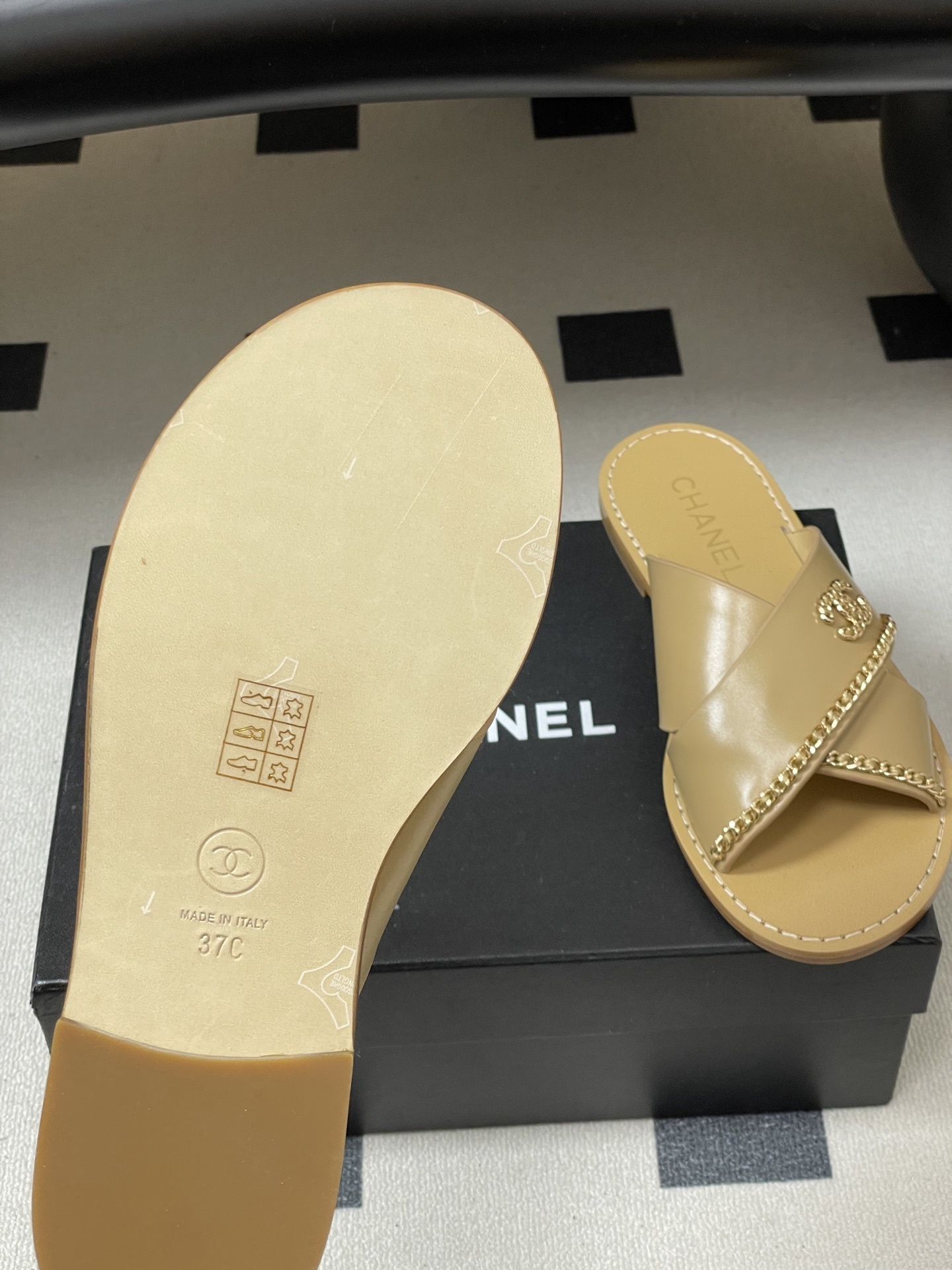 Pair of Chanel beige leather flat sandals with criss-cross straps and gold chain CC logo detailing on a black surface. - Hình 8