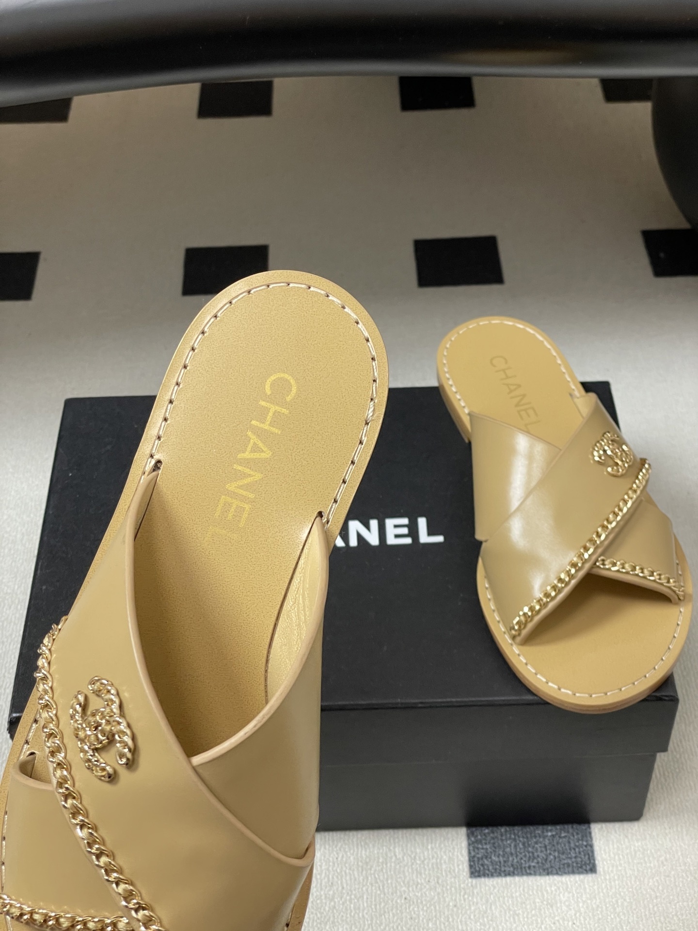 Pair of Chanel beige leather flat sandals with criss-cross straps and gold chain CC logo detailing on a black surface. - Hình 7