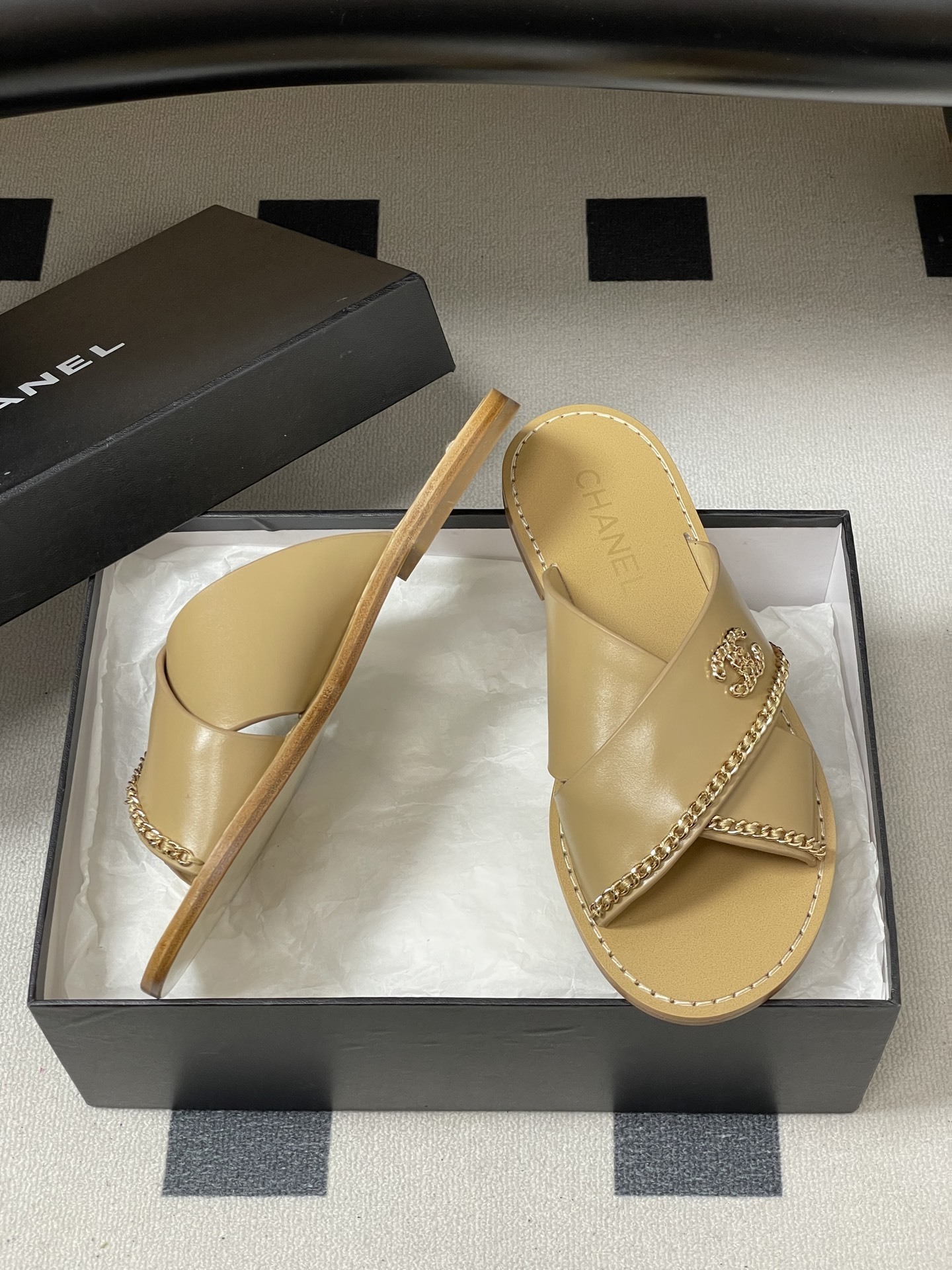 Pair of Chanel beige leather flat sandals with criss-cross straps and gold chain CC logo detailing on a black surface. - Hình 6