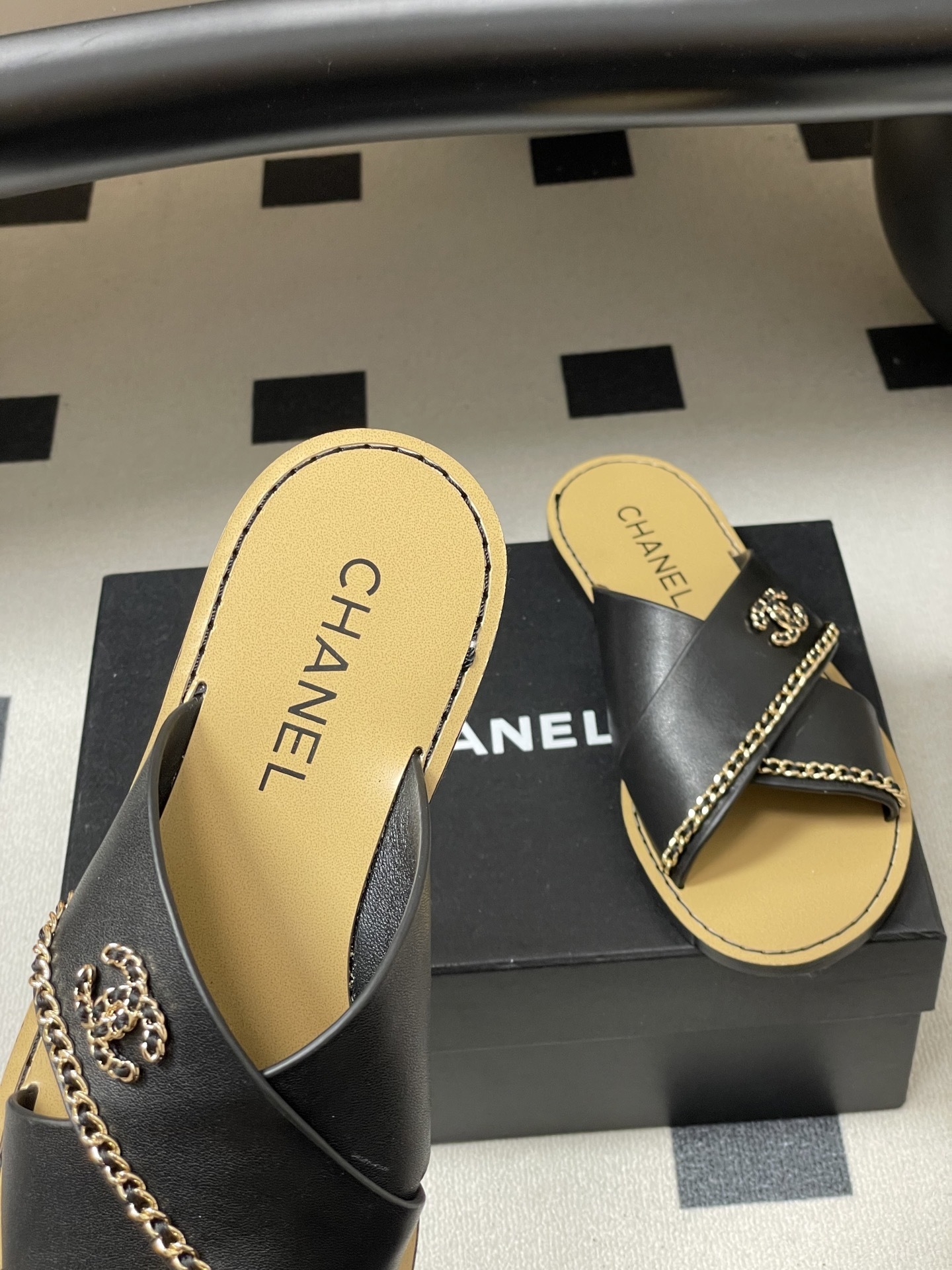 Pair of Chanel black leather criss-cross flat sandals with gold chain accents and interlocking CC logo on a black surface. - Hình 7