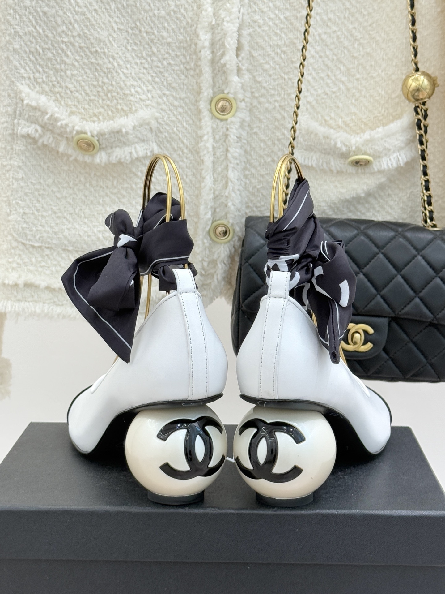 Elegant white and black two-tone pumps featuring a unique pearl sphere heel and a black silk scarf ankle tie, resting on a black designer box. - Hình 6