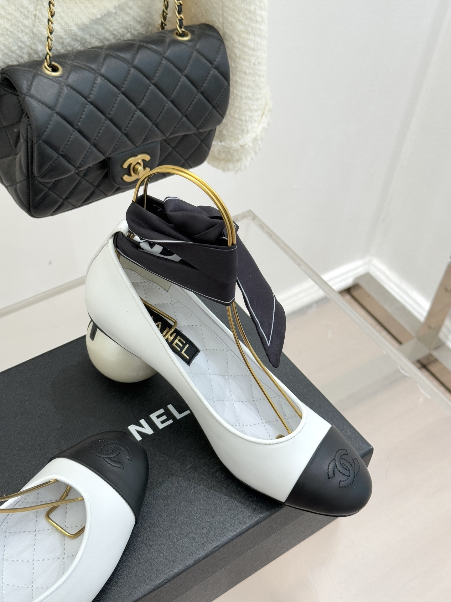 Elegant white and black two-tone pumps featuring a unique pearl sphere heel and a black silk scarf ankle tie, resting on a black designer box. - Hình 5