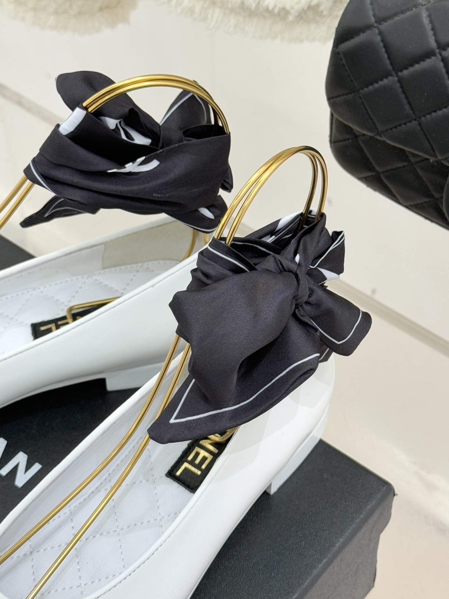Luxury white Chanel ballerina flats with black toe caps and black silk ribbon bows displayed on a black brand box. - Hình 8
